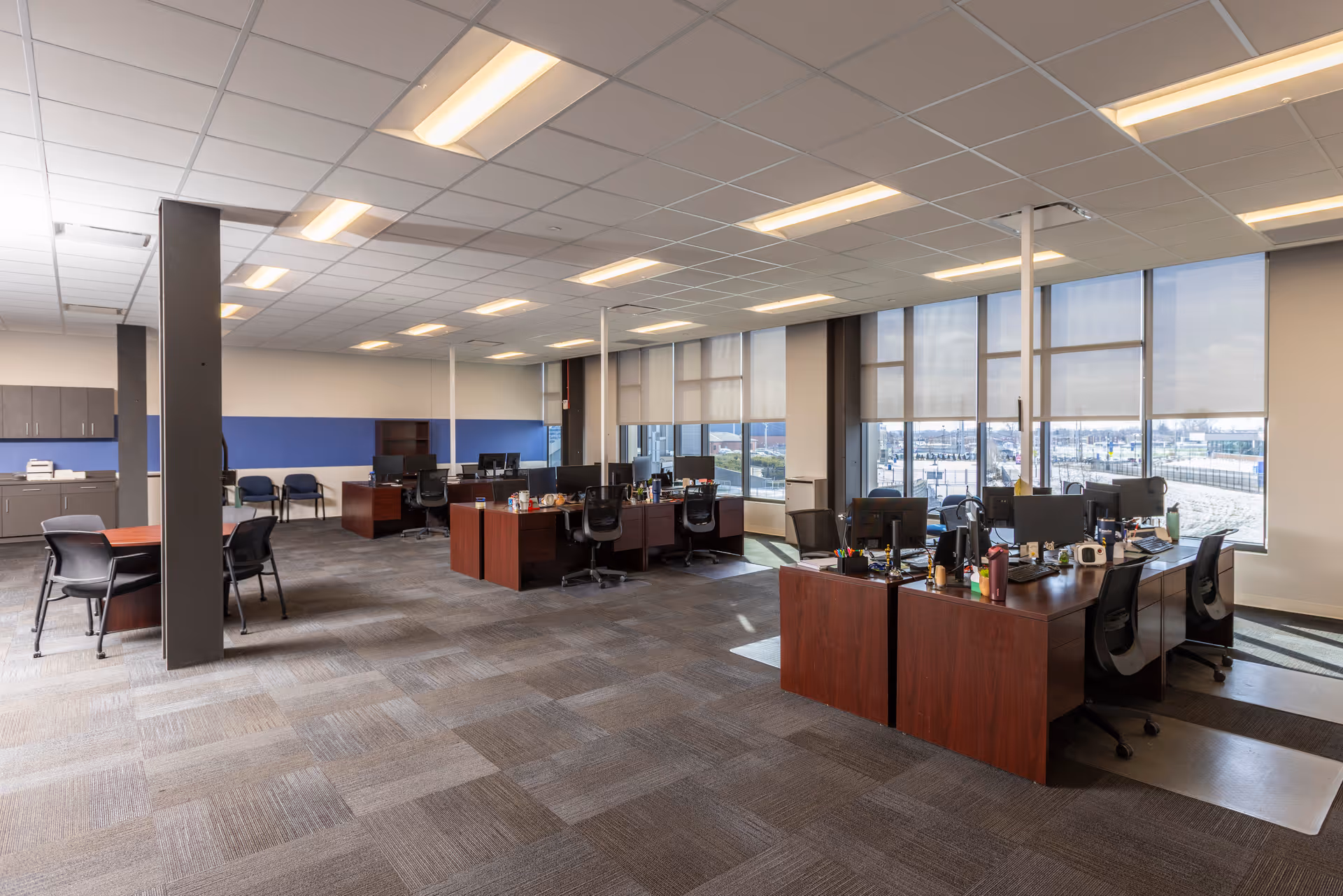 Open office area with desks, computers, chairs, and expansive windows overlooking the city.