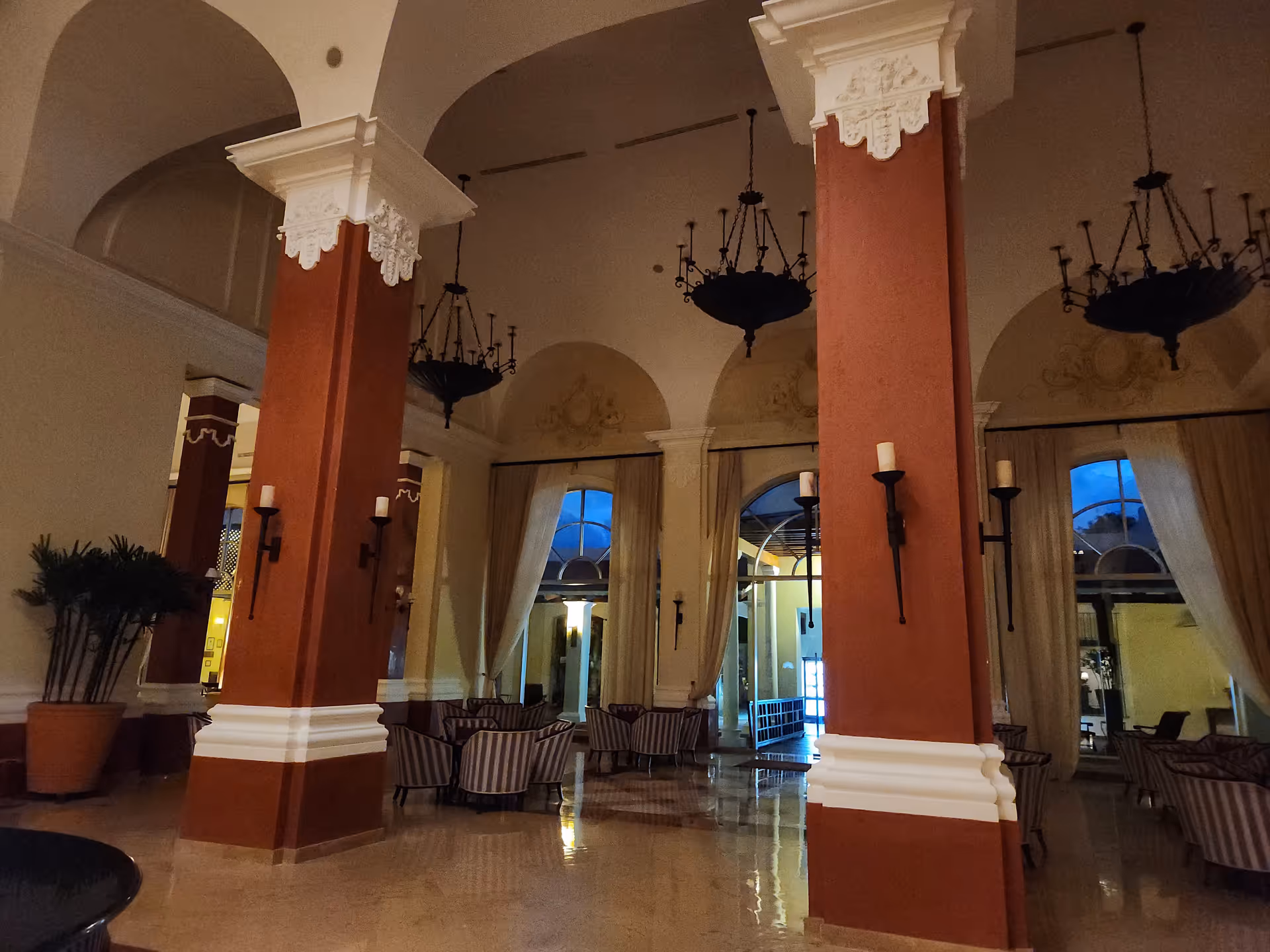 Spacious lobby with tall columns, arches, chandeliers, and seating.