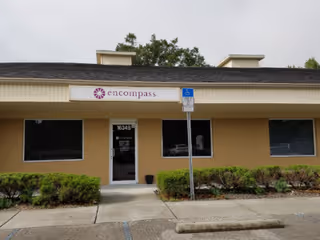 Front view of a single-story beige facility with an Encompass sign and shrubs.
