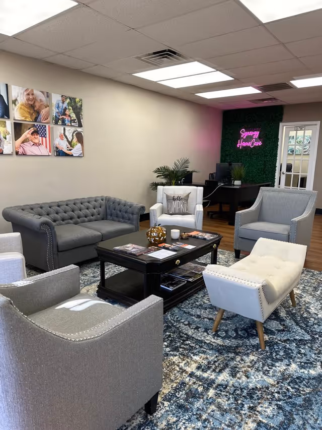Modern waiting area in a Synergy HomeCare facility with couches, chairs, and a neon sign.