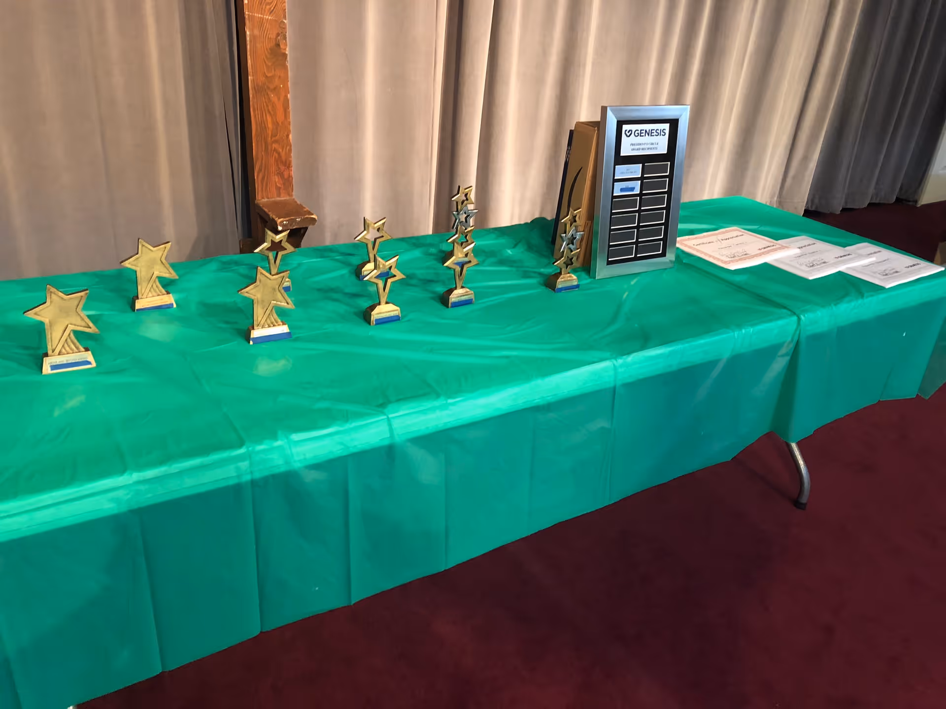 A table with green cloth displays multiple star-shaped trophies and a plaque indoors.