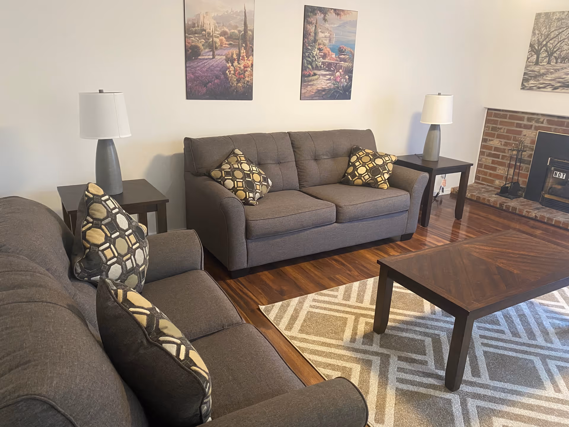 Cozy living room in a senior facility with gray sofas, lamps, coffee table, and fireplace.