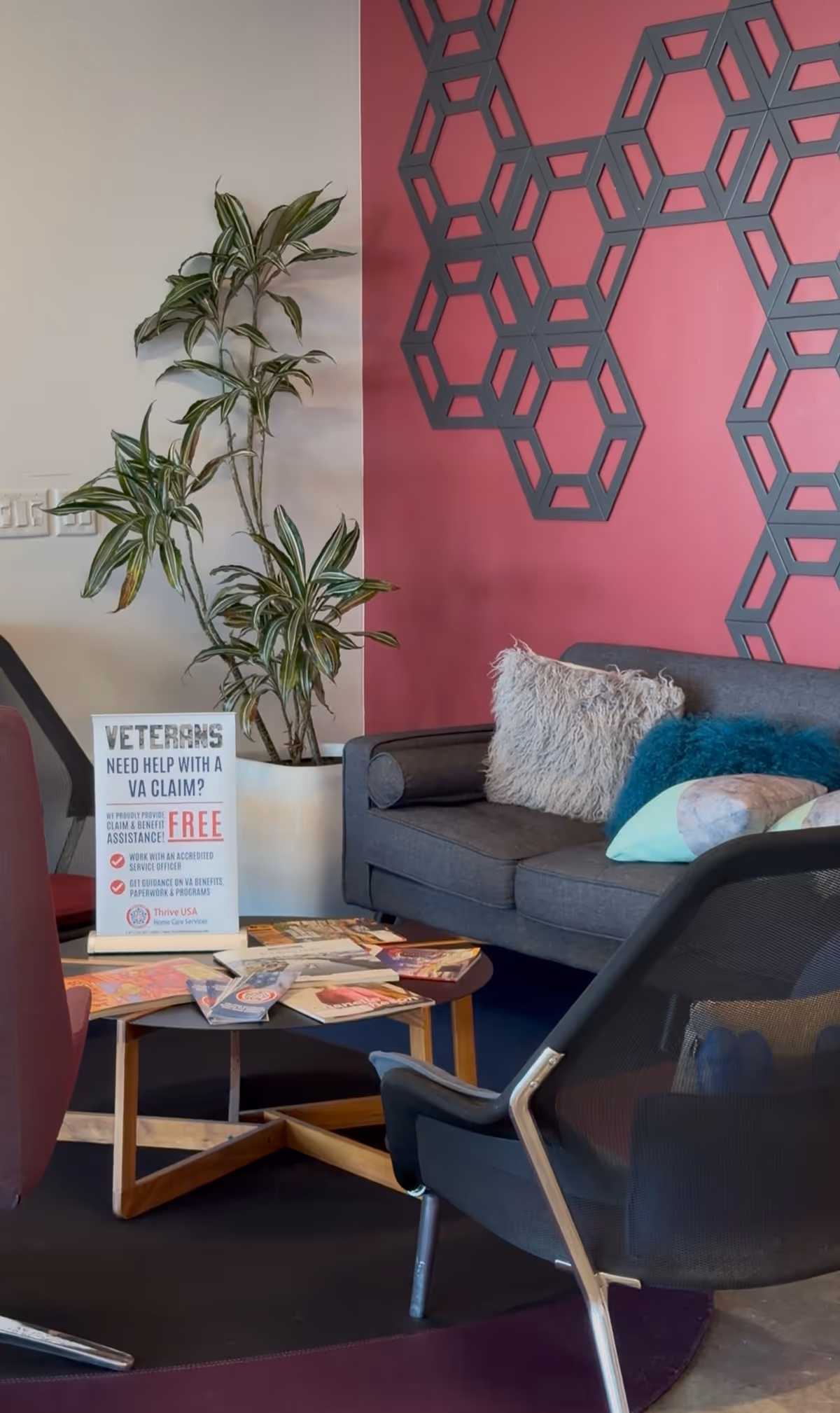 Modern living room corner with pink geometric wall, sofa, plant, and brochures.
