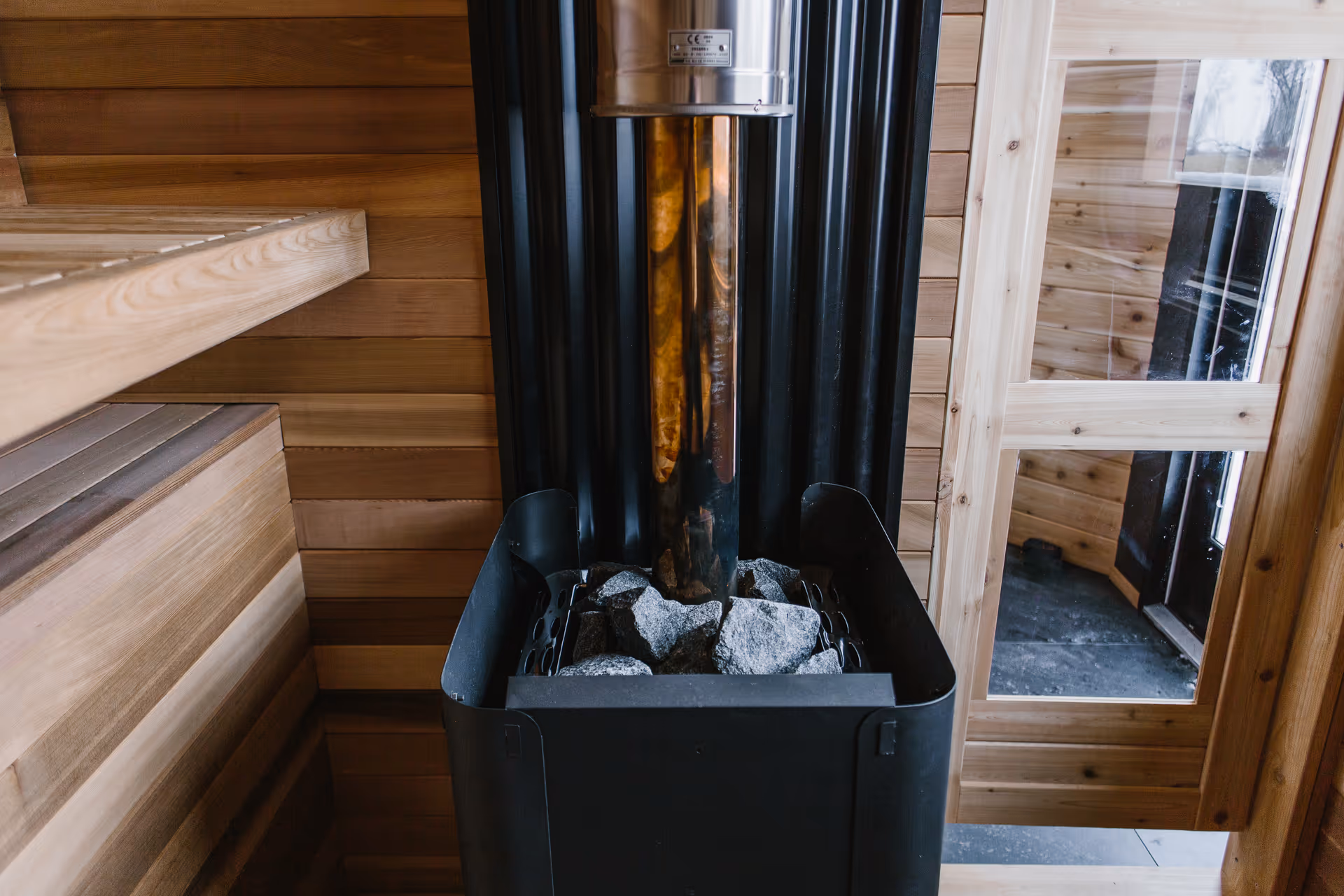 Wood-paneled sauna interior with a metal heater and stacked rocks.