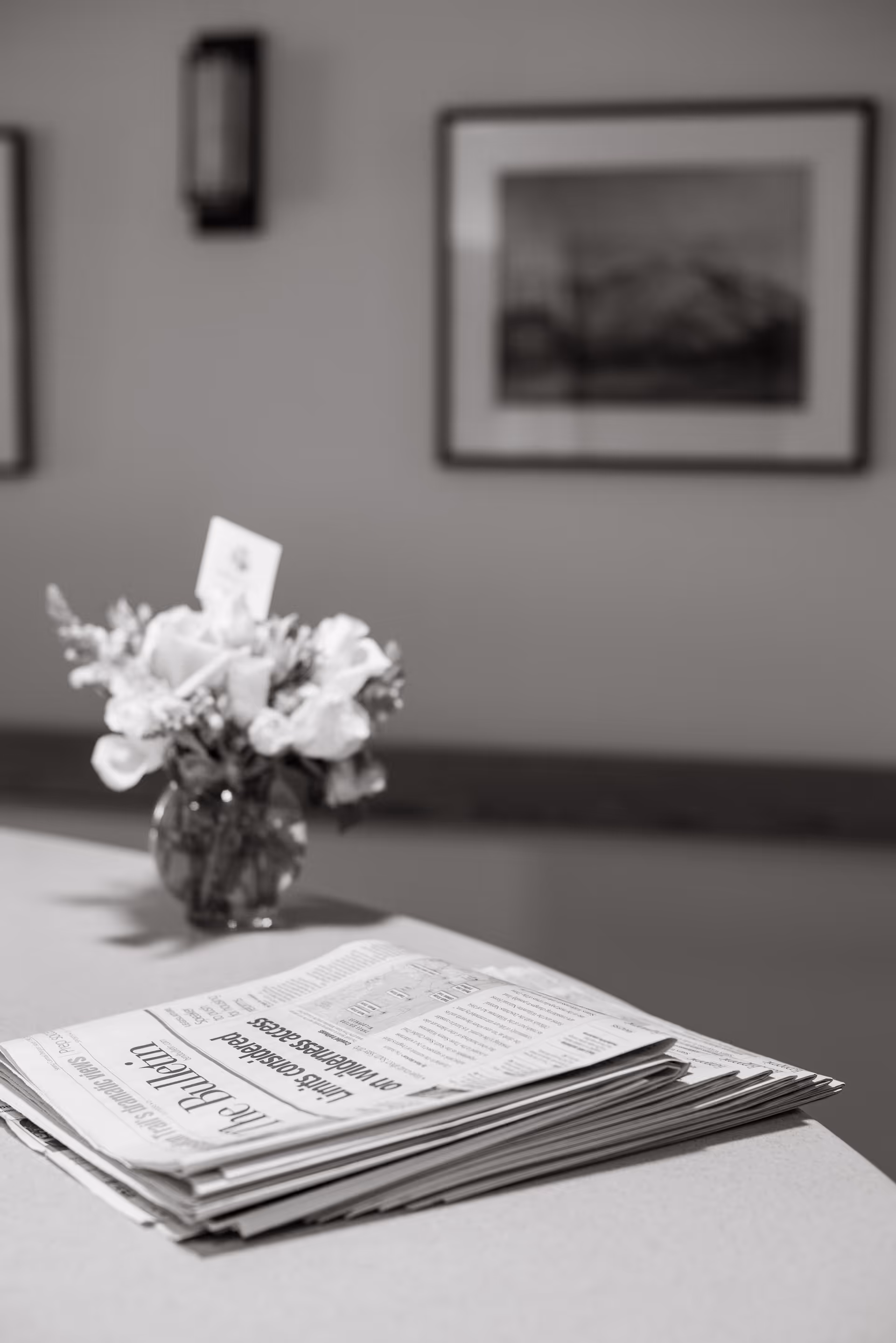 Indoor reception area with a vase of flowers and a stack of newspapers on a table.