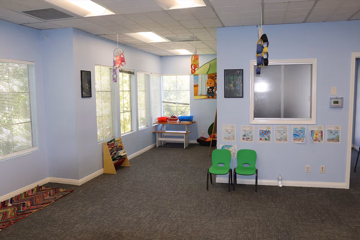 Bright blue interior activity room with windows, two green chairs, and children's artwork on walls.
