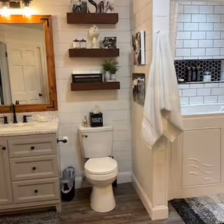 Compact bathroom with white vanity, mirror, toilet, shelves, and a tiled shower.