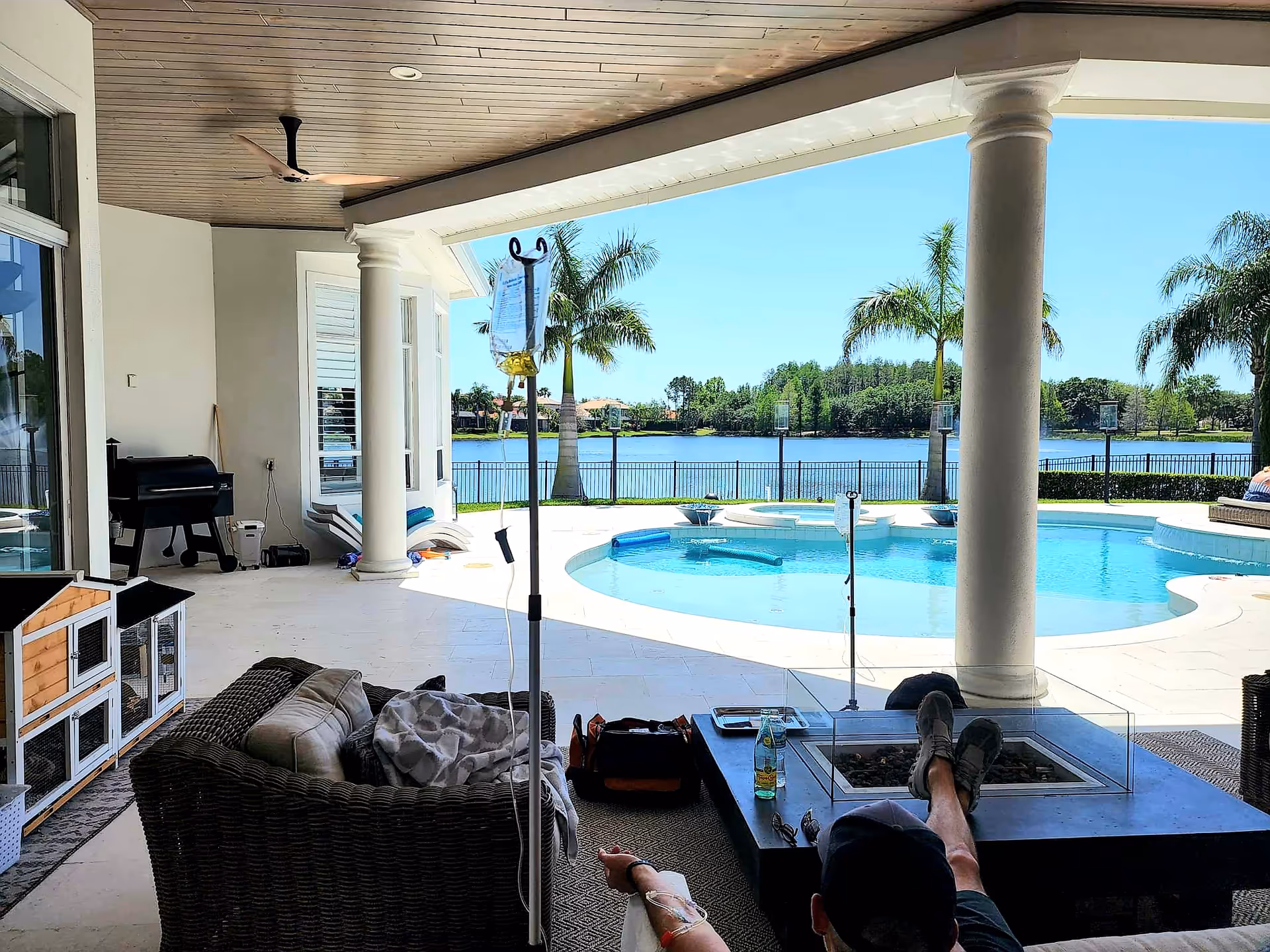 Covered patio overlooking a pool and lake, with seating and a person relaxing.
