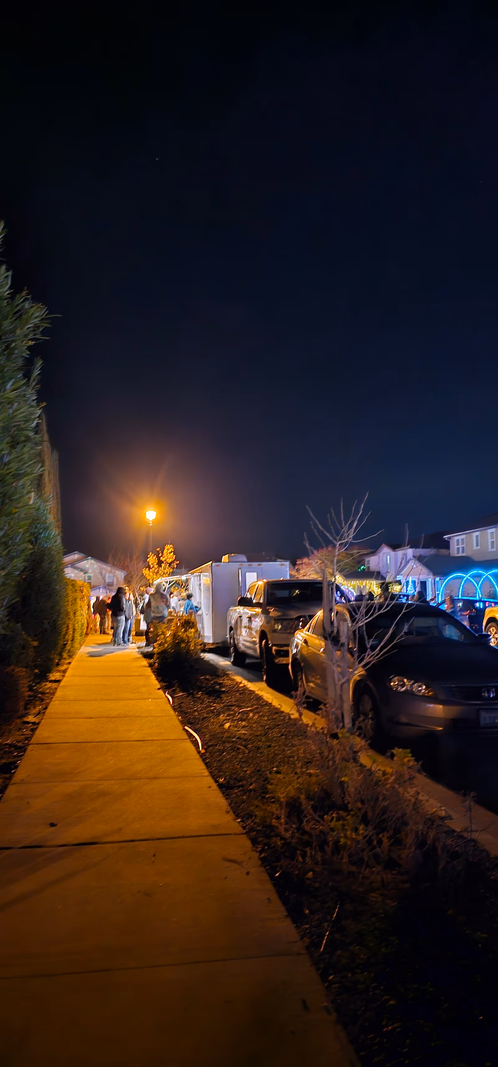 Night exterior view of a walkway beside a building with parked cars.