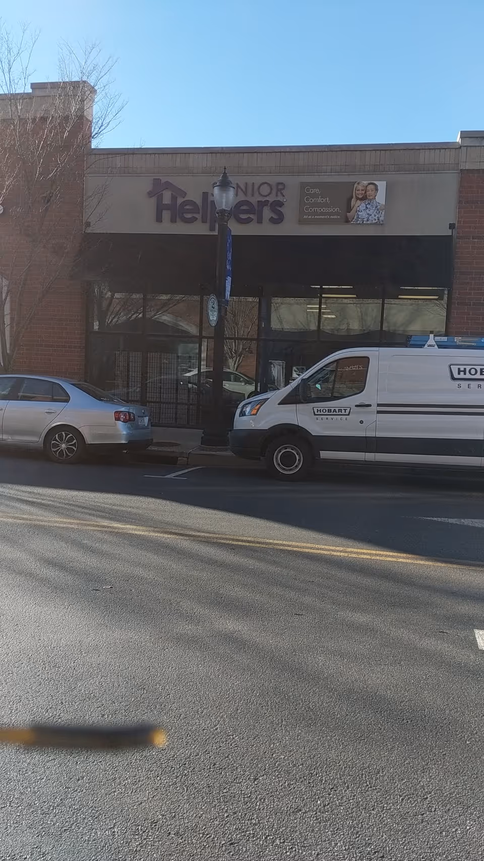 Exterior view of Senior Helpers facility with sign, brick storefront, and parked vehicles.