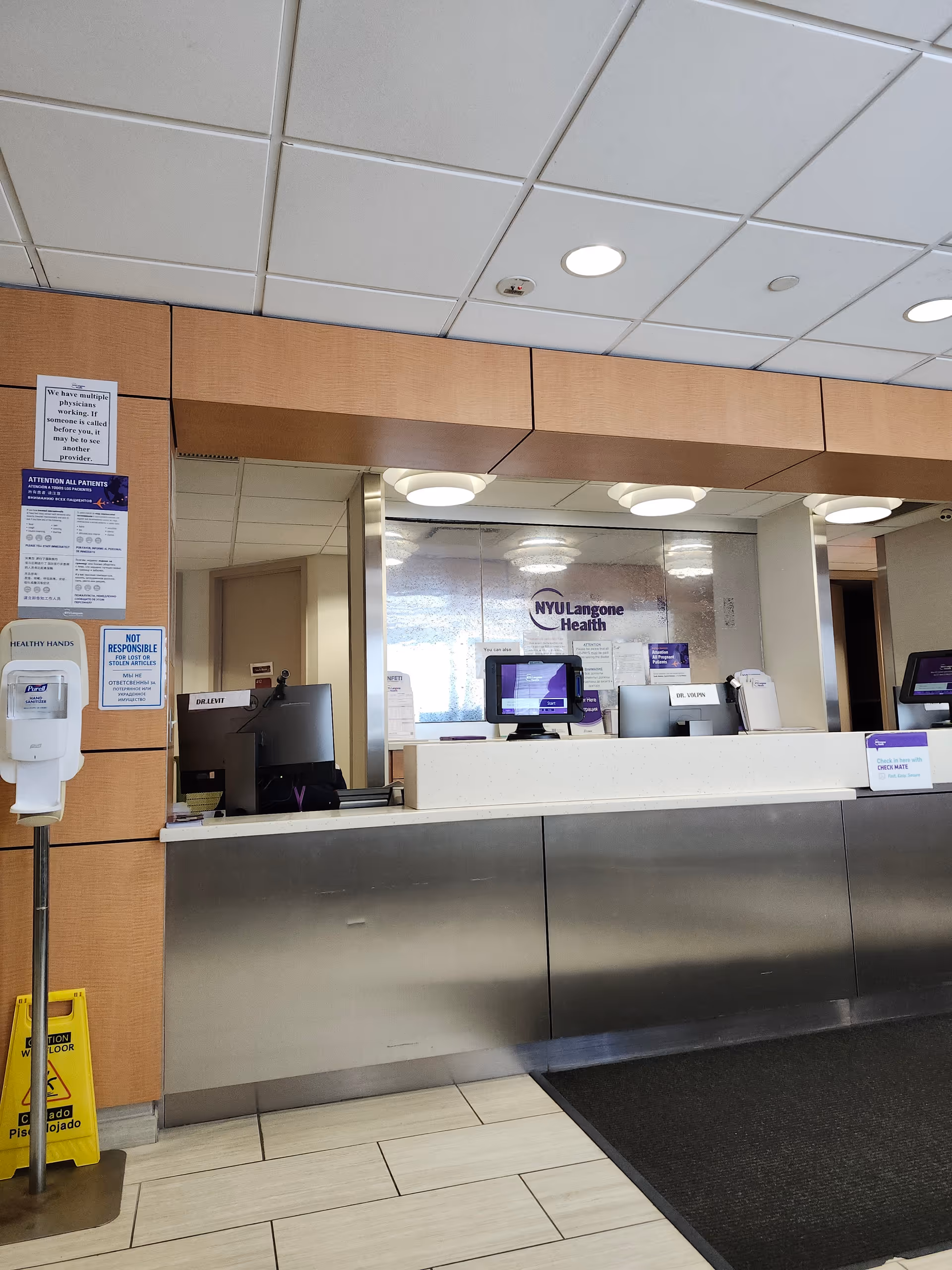 Lobby reception desk with computers and NYU Langone Health logo, wood panels, tiled floor.