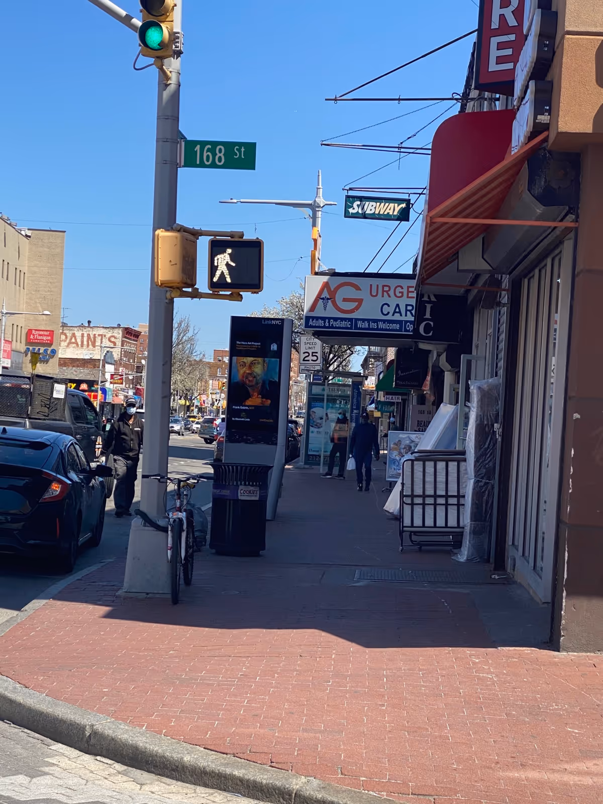 Sunny city street scene with traffic light, crosswalk signal, and row of storefronts.