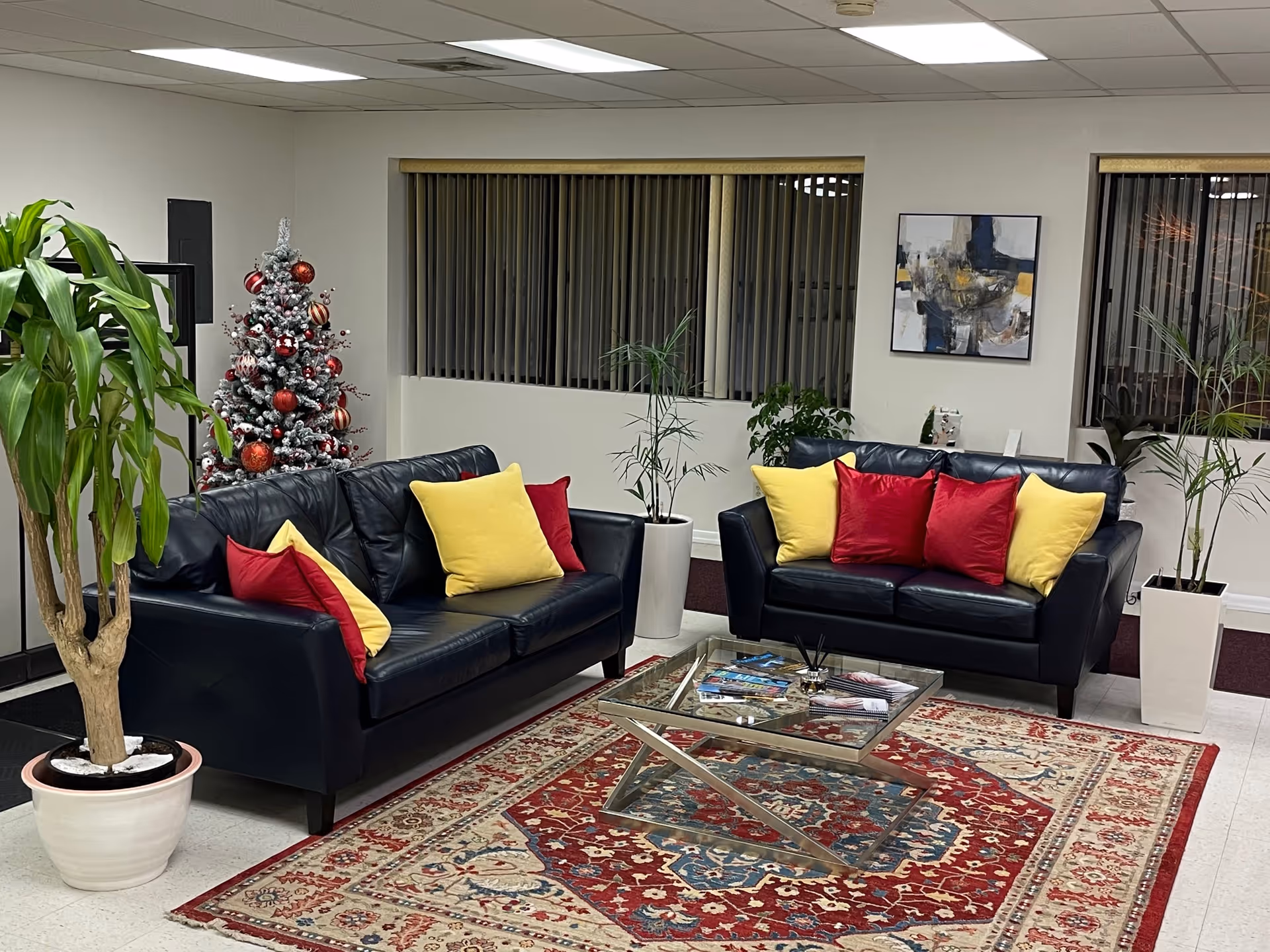 Reception-style lounge with black leather couches, colorful pillows, a glass coffee table, and a Christmas tree.