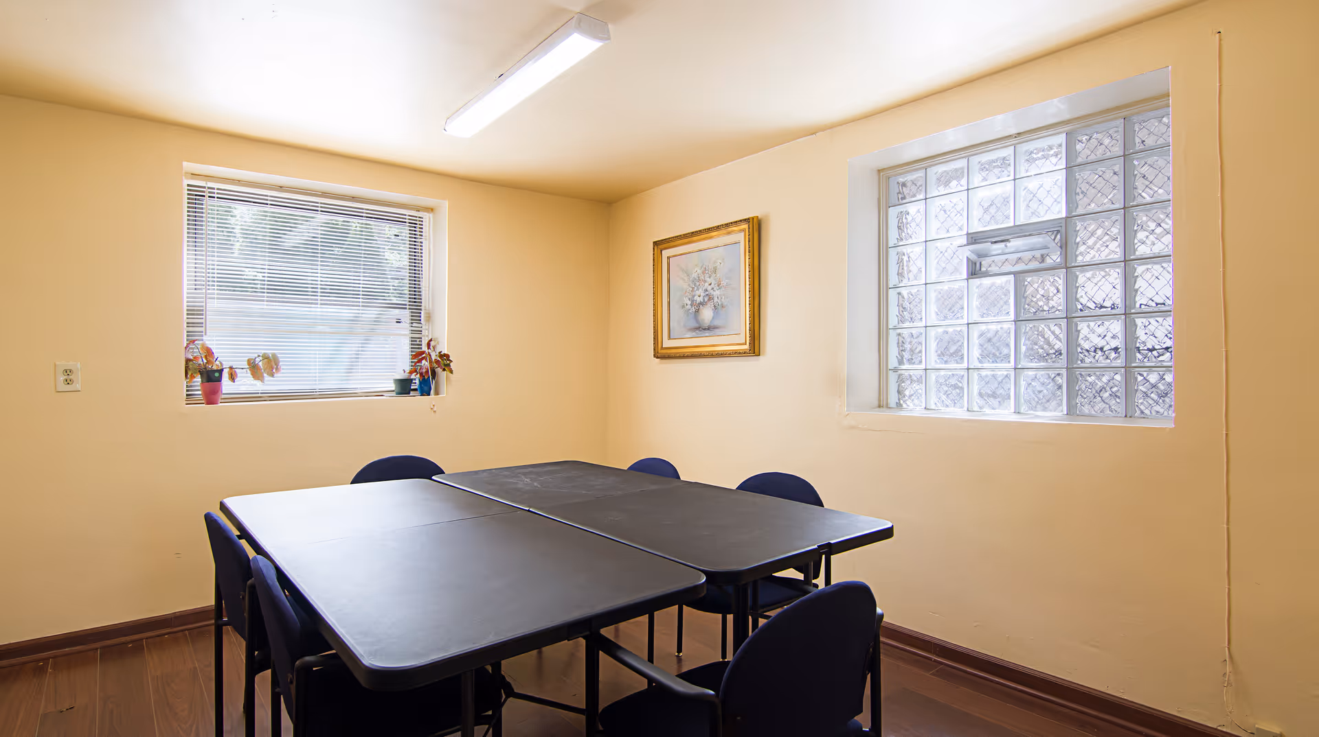 A small beige dining room with a table, blue chairs, and windows.