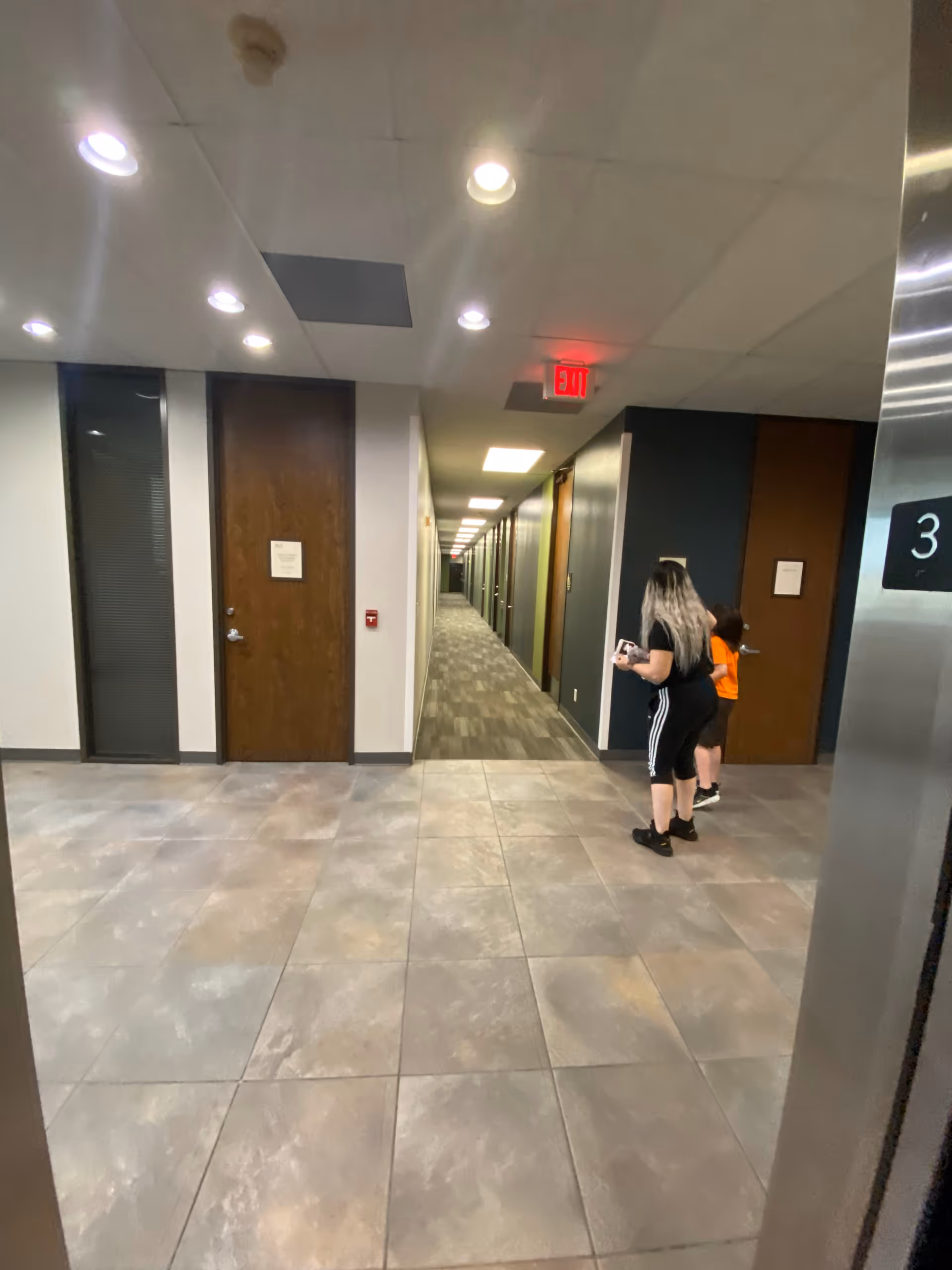 Long hallway inside a senior living facility with doors, ceiling lights, and two people.
