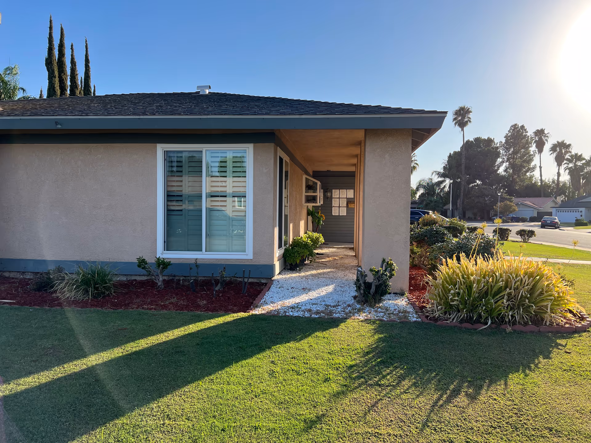 Single story beige building with a walkway, window, and landscaped front yard.