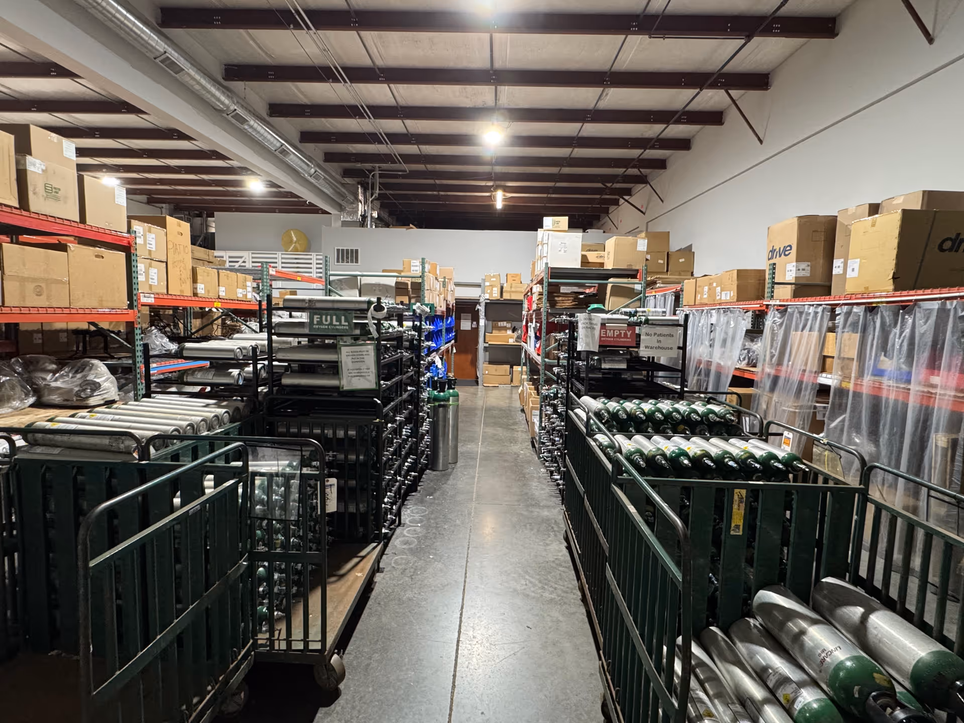 Long aisle of a warehouse storage room with metal shelves, boxes, and carts.