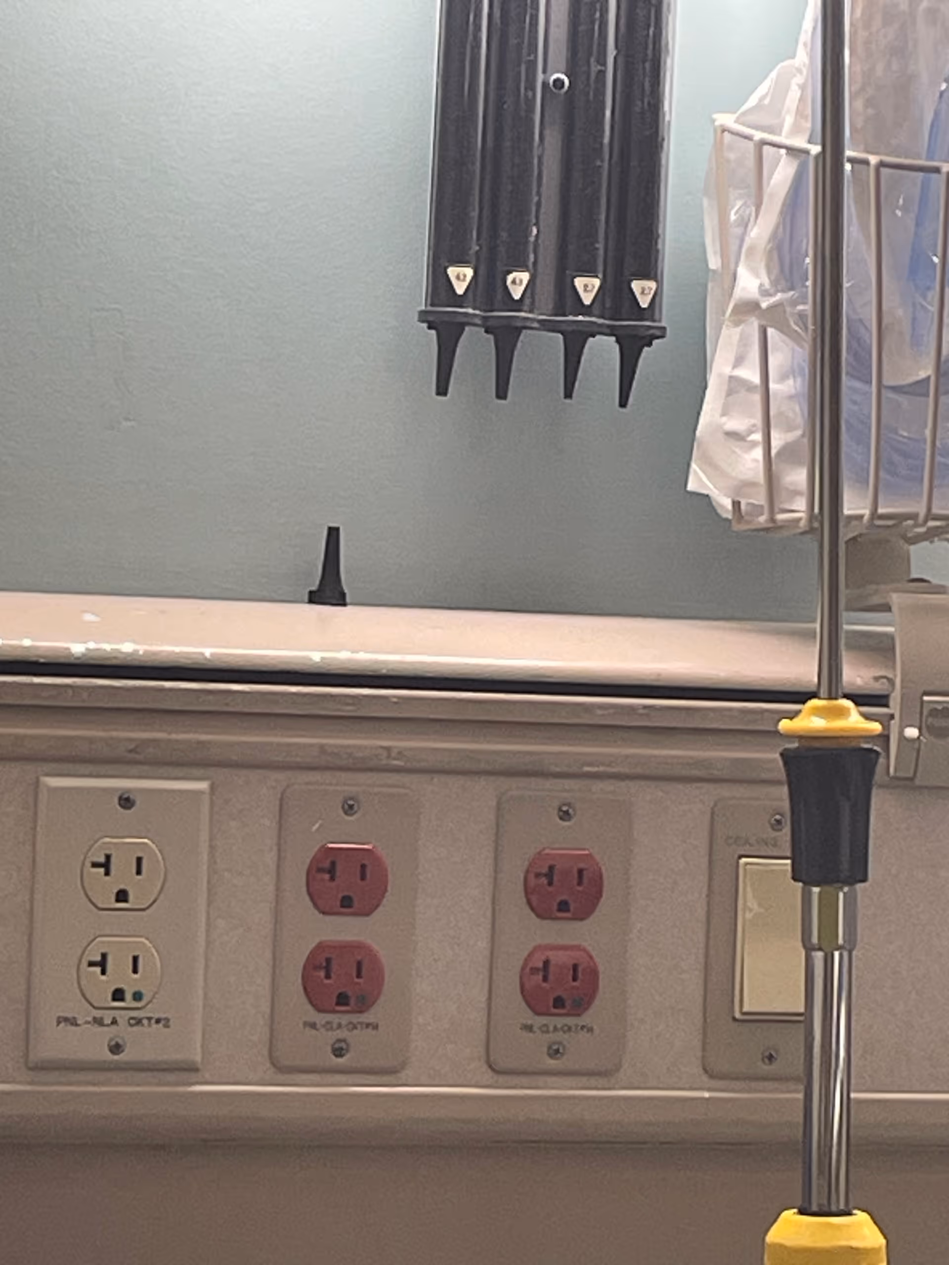 Close view of a hospital room wall with outlets, IV pole, and bed rail.