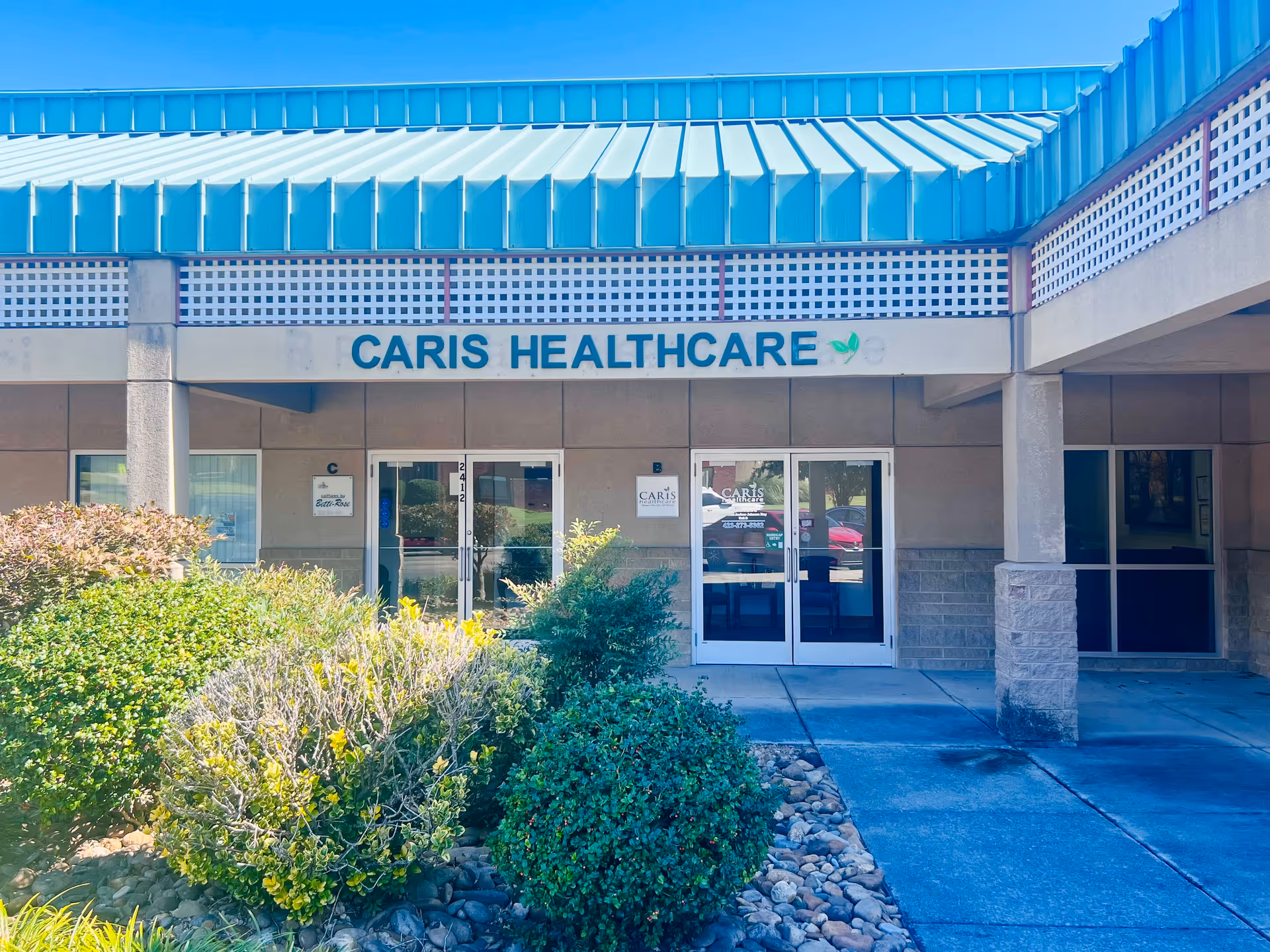 Front entrance of Caris Healthcare with glass doors and landscaped shrubs.