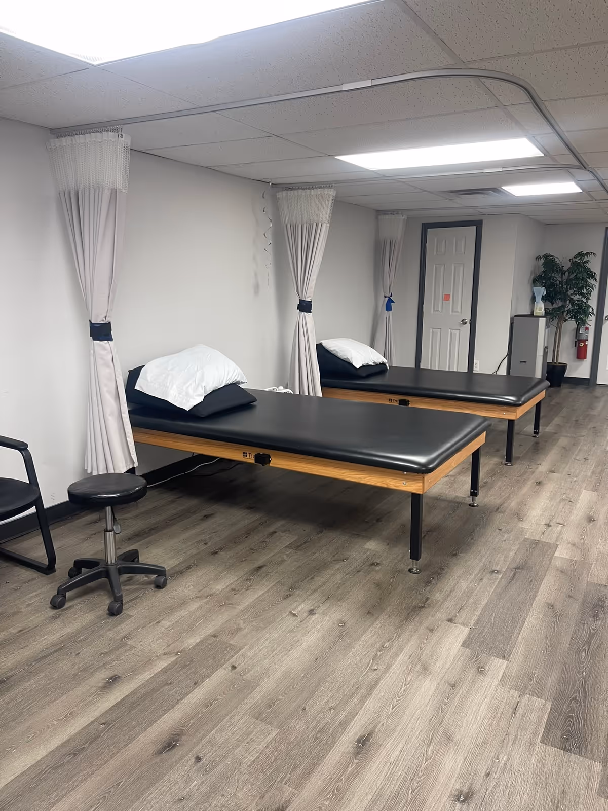 A rehabilitation room with two therapy beds, privacy curtains, and seating in a facility.