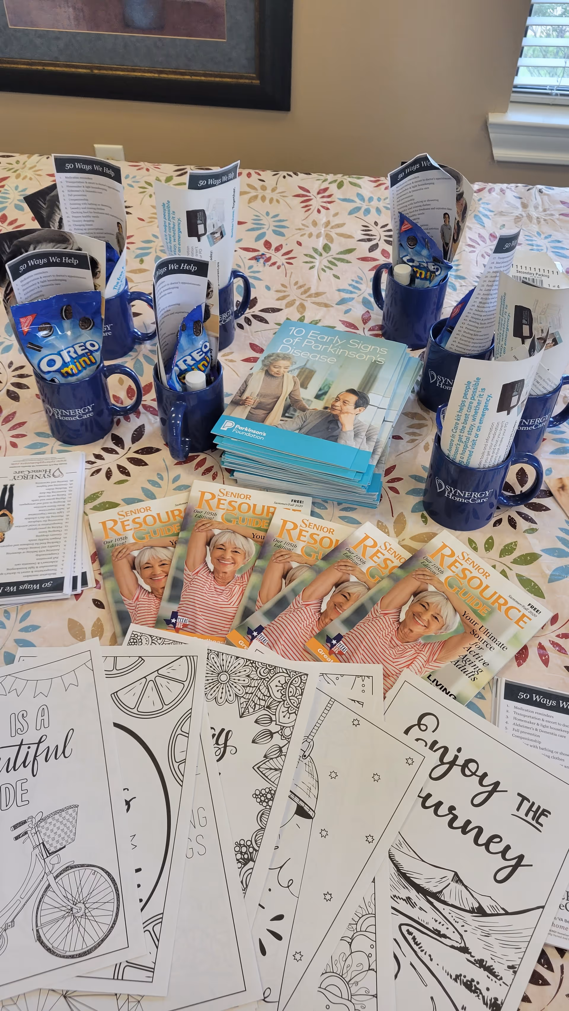 Table with brochures, magazines, coloring pages, and blue mugs inside a decorated room.