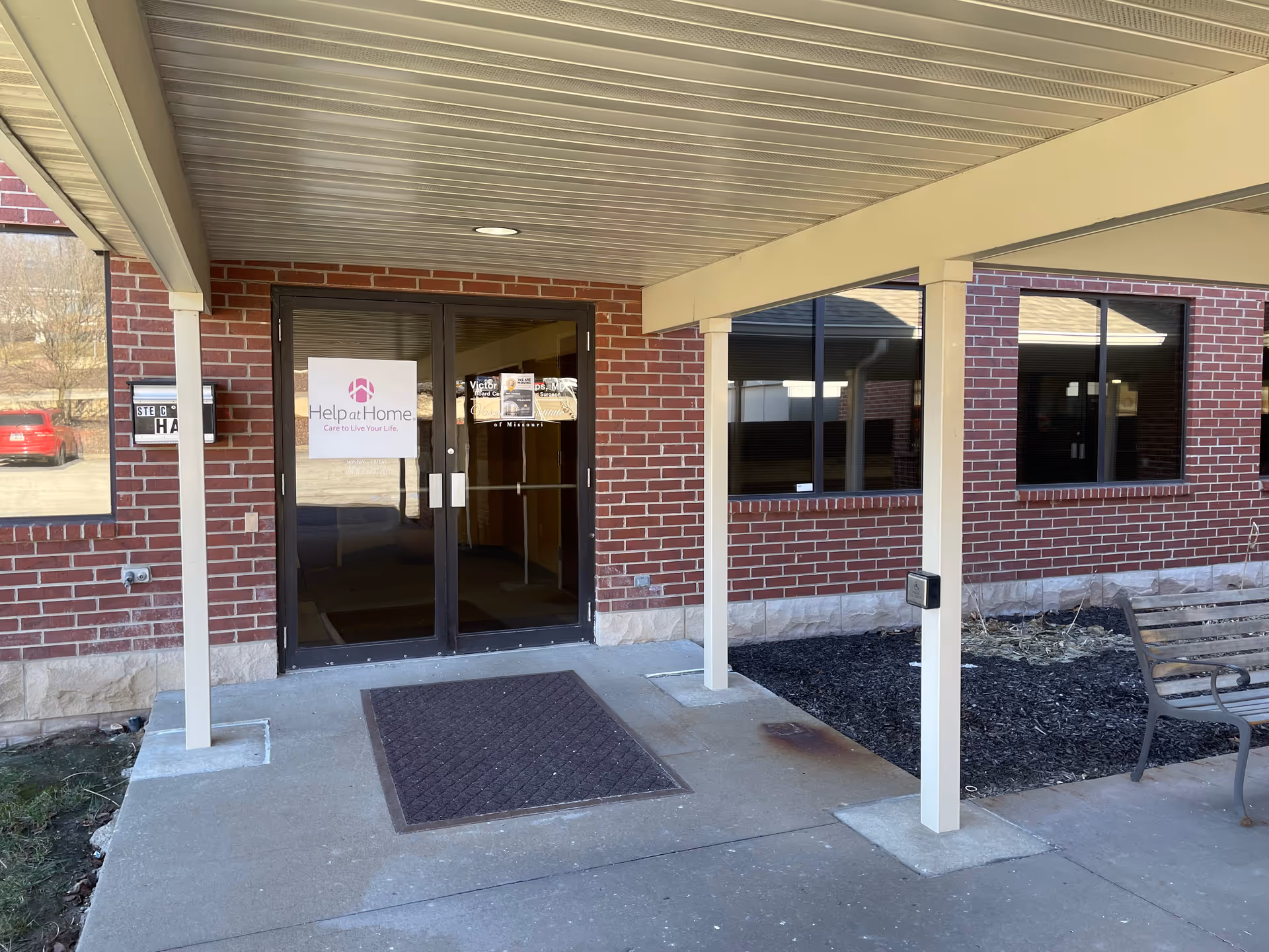 Brick building exterior with glass doors labeled Help at Home under a covered entrance.