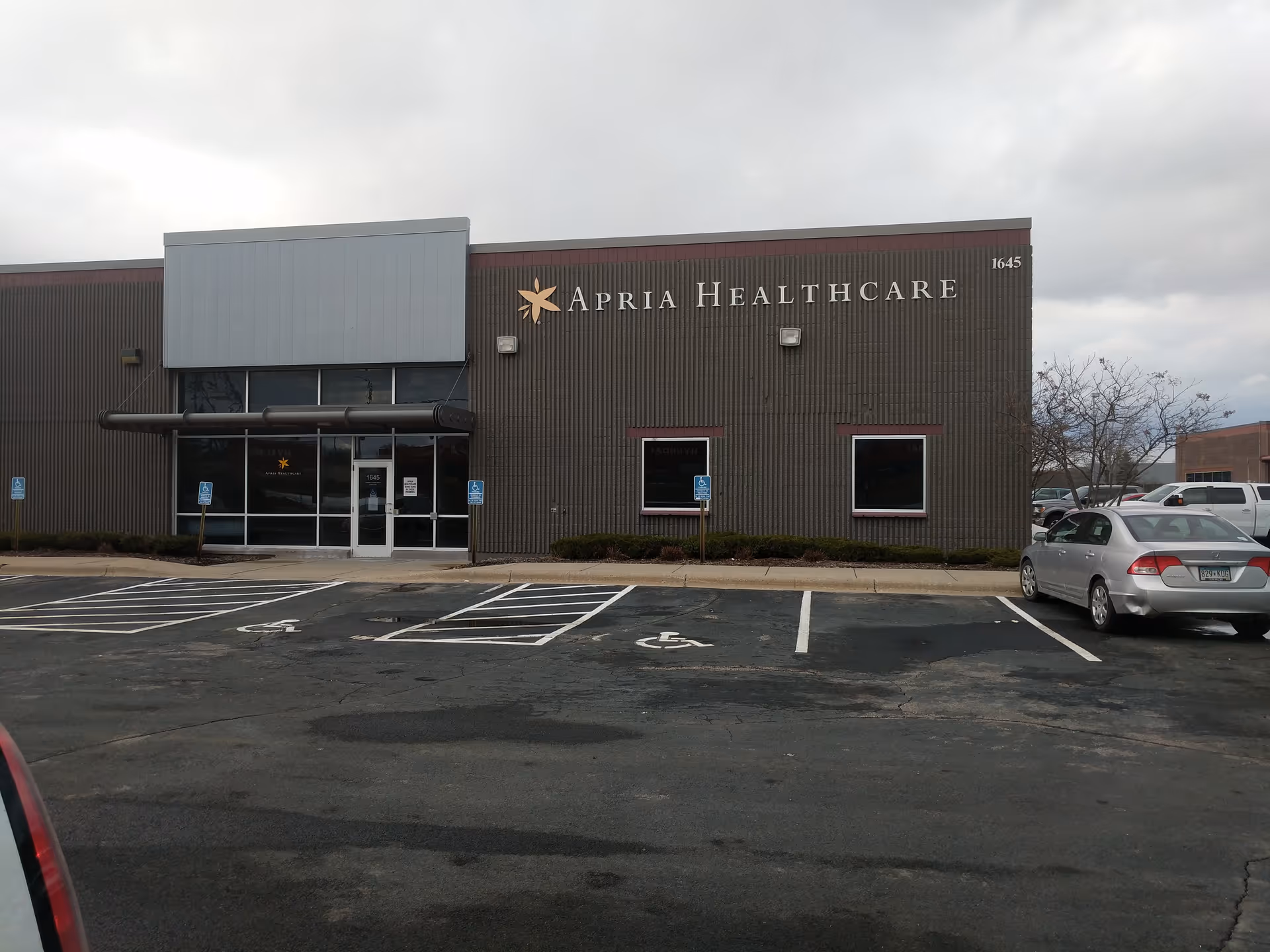 Exterior view of an Apria Healthcare building with a glass entrance and parking lot.