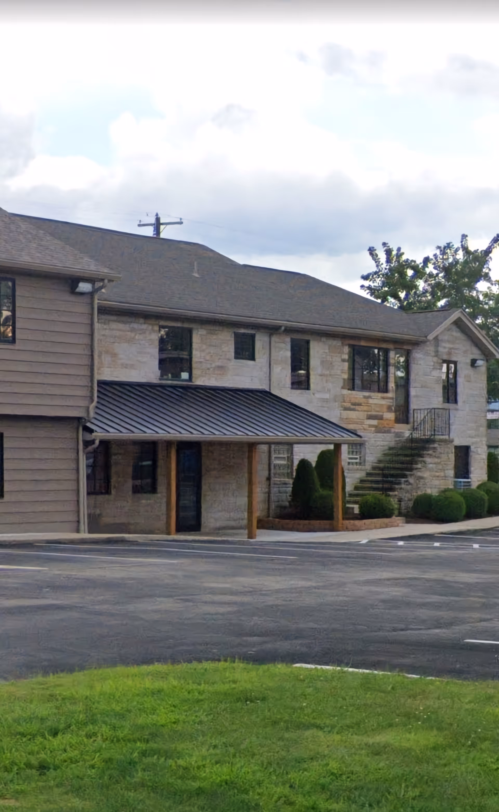 Exterior view of a two-story stone-and-wood building with a front entrance and parking.