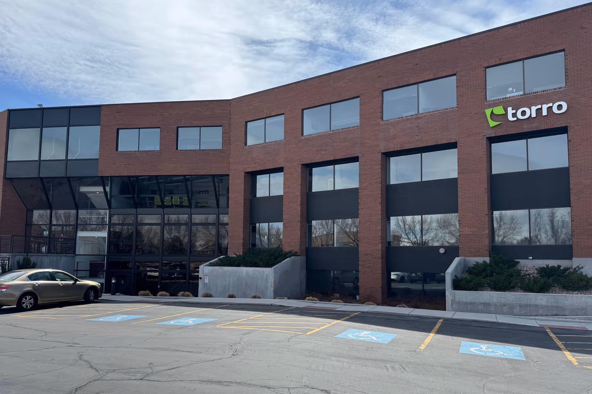 Brick building with large windows and glass entrance, torro sign, parking in front.