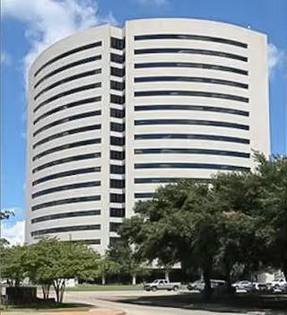 Tall curved white office building with trees and parked cars.