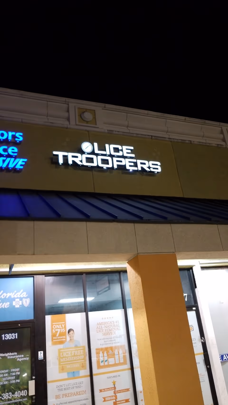 Nighttime exterior of a building with a bright Lice Troopers sign above the storefront.