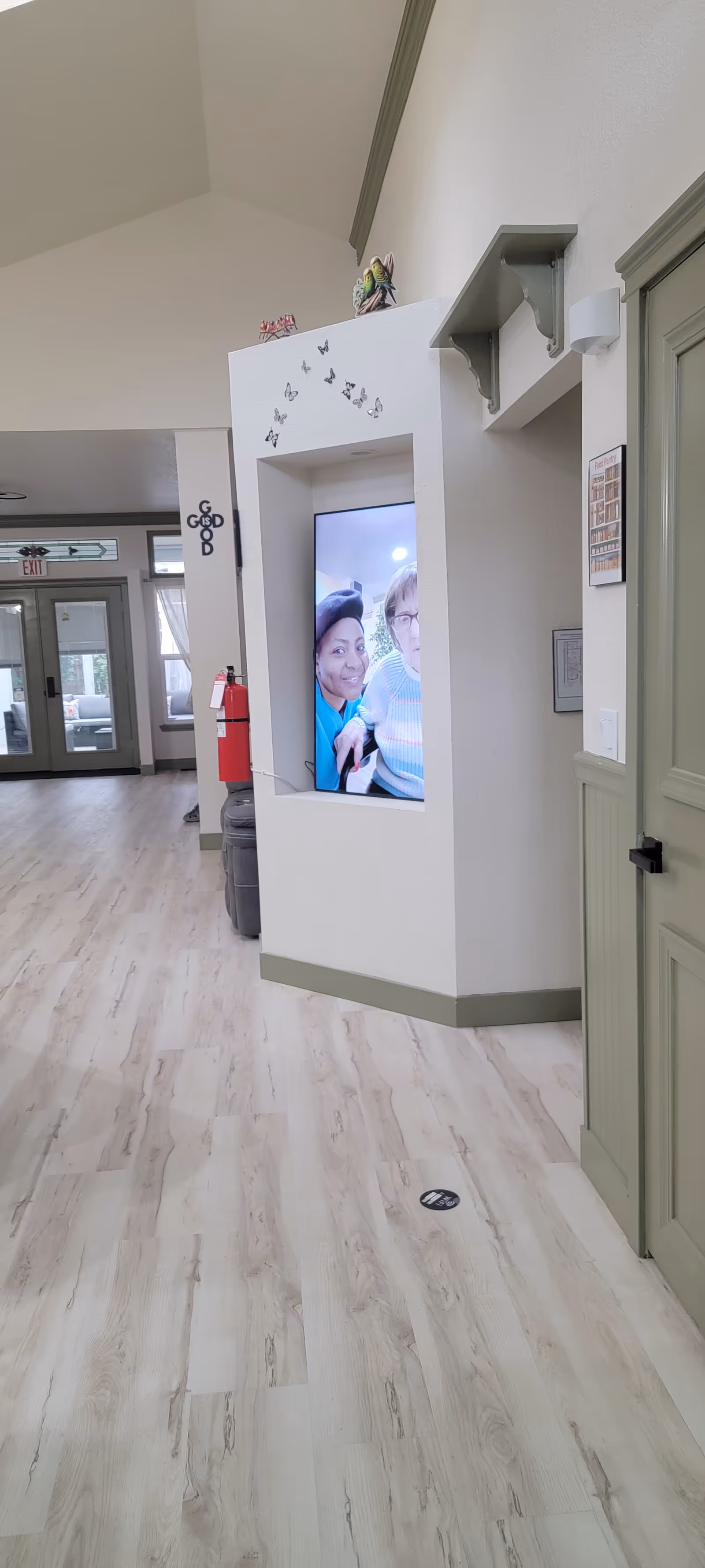 Bright interior hallway of a senior living facility with a wall-mounted display screen.