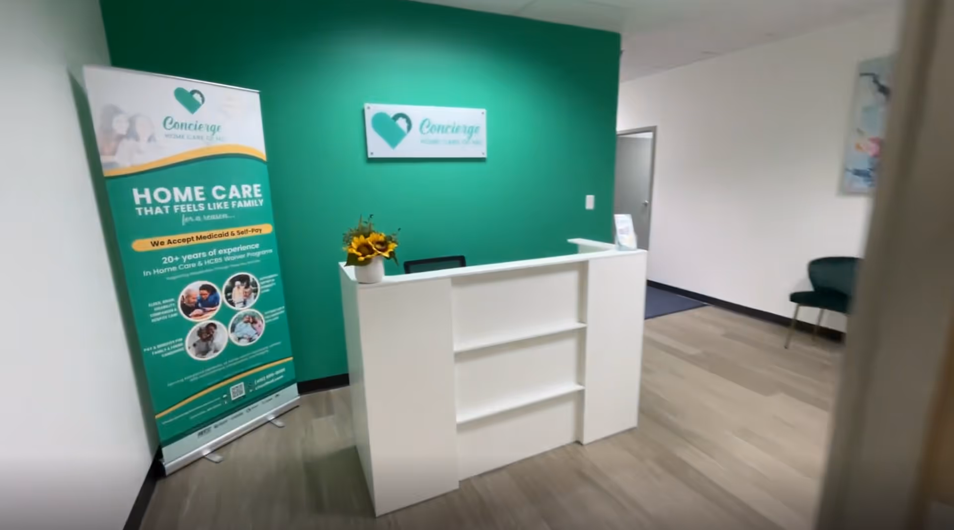 Reception desk in a green-walled lobby with a banner and seating area.