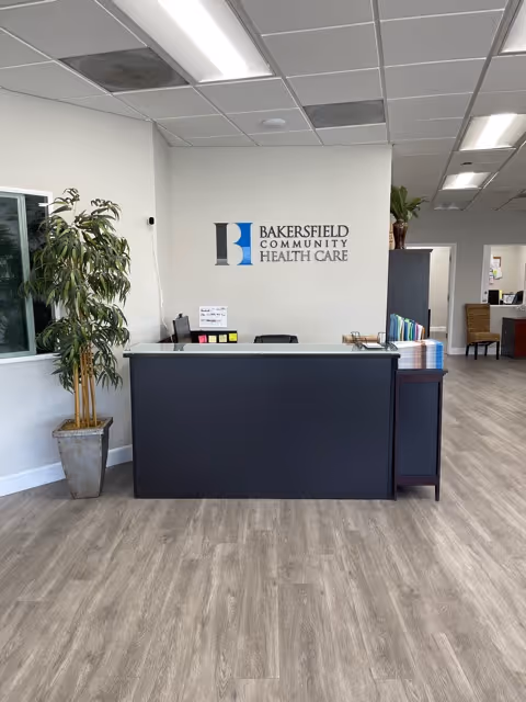 Reception desk in a medical facility lobby with plants and a Bakersfield Community Health Care sign.