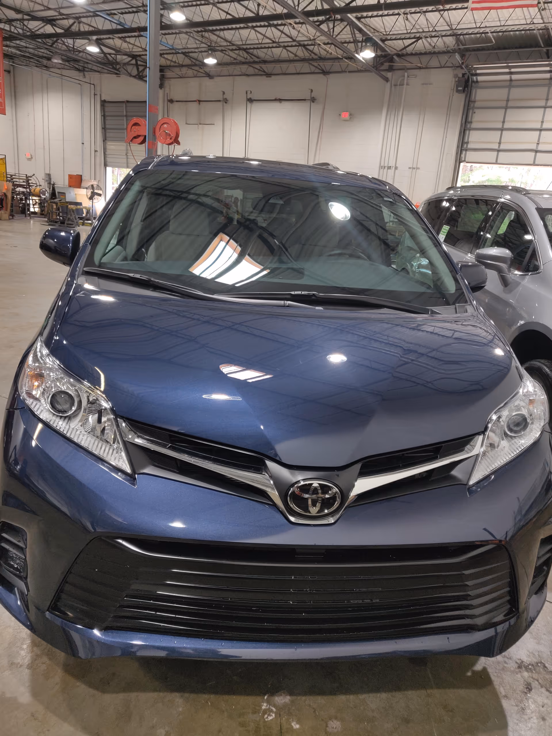 Blue Toyota minivan parked inside a large indoor service workshop.