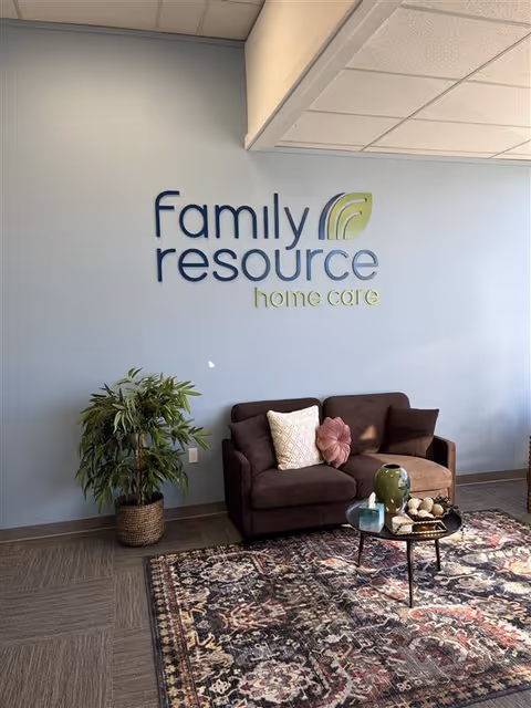 Lobby area with a blue wall, Family Resource Home Care sign, brown sofa, and plant.