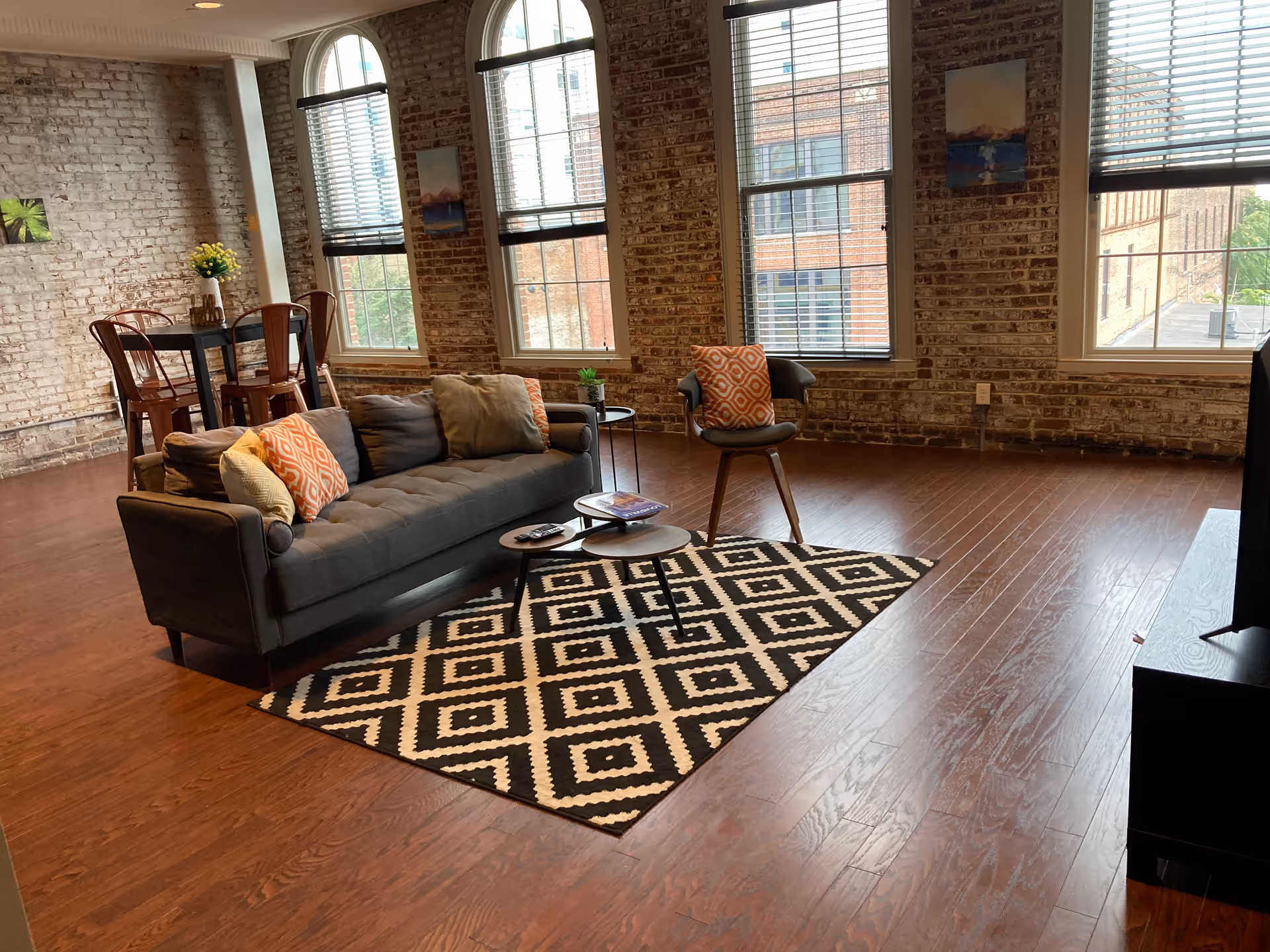 Brick-walled lounge with sofa, chairs, coffee table, and large windows.