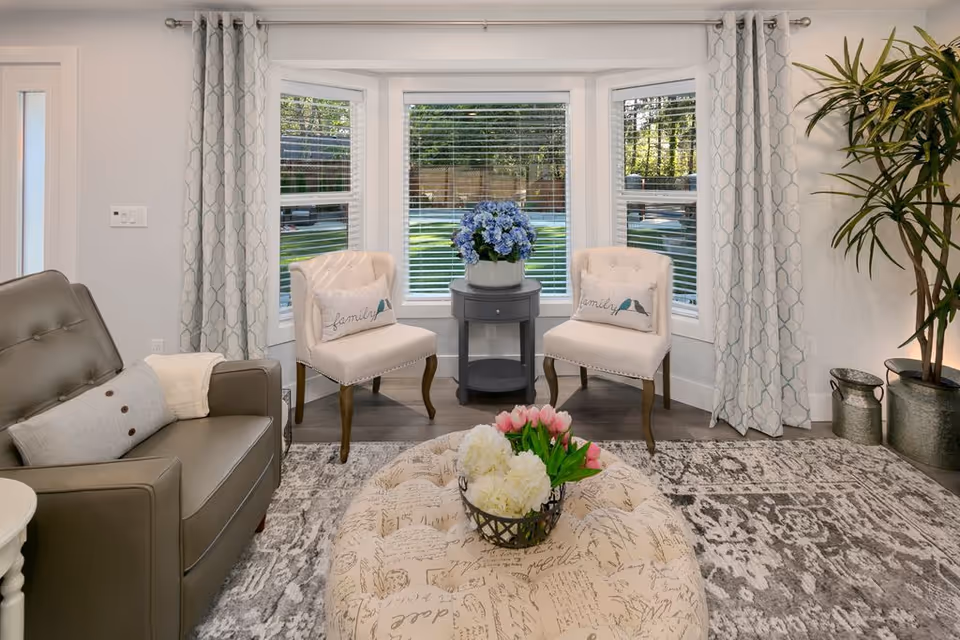 Bright living room with two upholstered chairs, a sofa, ottoman, and potted plants.
