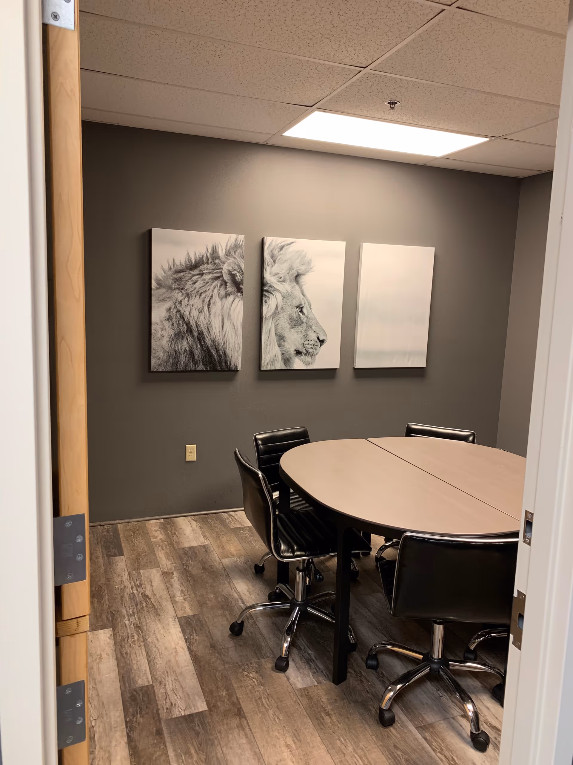 Small conference room with oval table, black chairs, gray walls, and three-panel lion artworks.