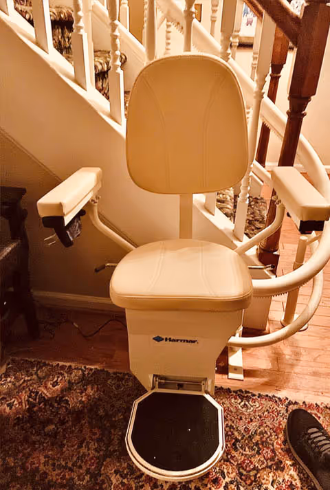 Cream stair lift chair installed on an indoor wooden staircase beside railings.