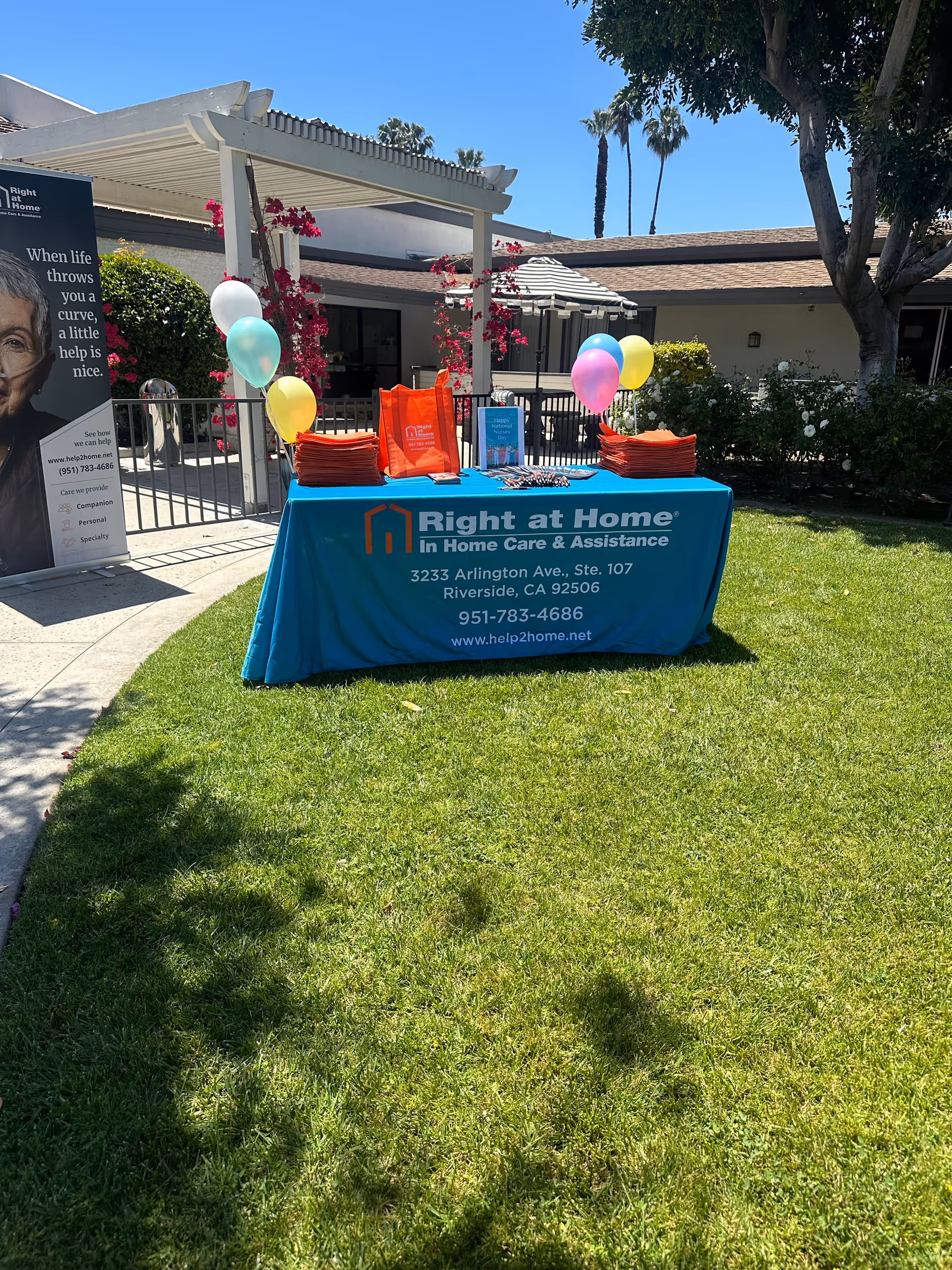 Outdoor promotional table with Right at Home banner and balloons in courtyard.