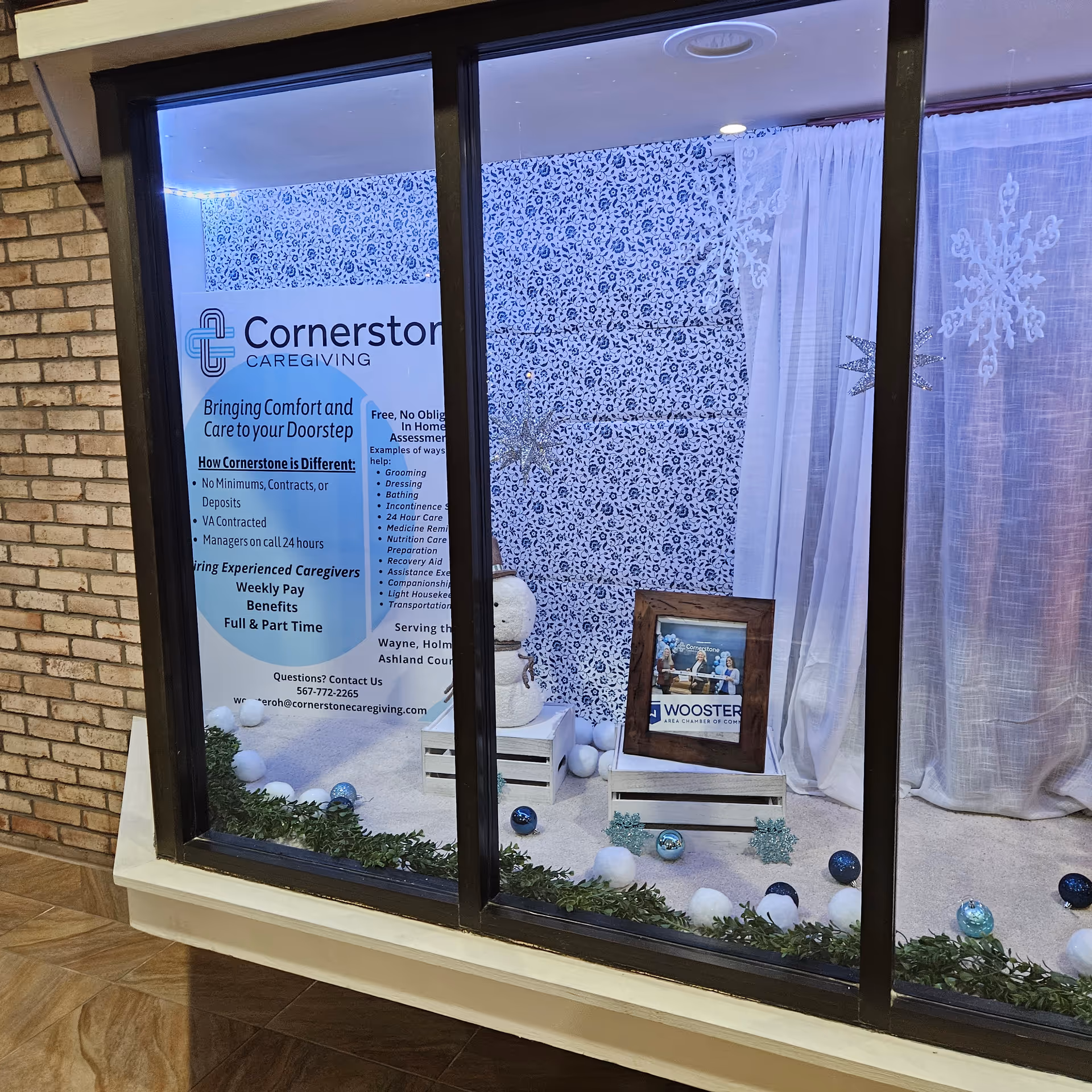 Storefront window display for Cornerstone Caregiving with a poster, blue wallpaper, and snowflake decor.