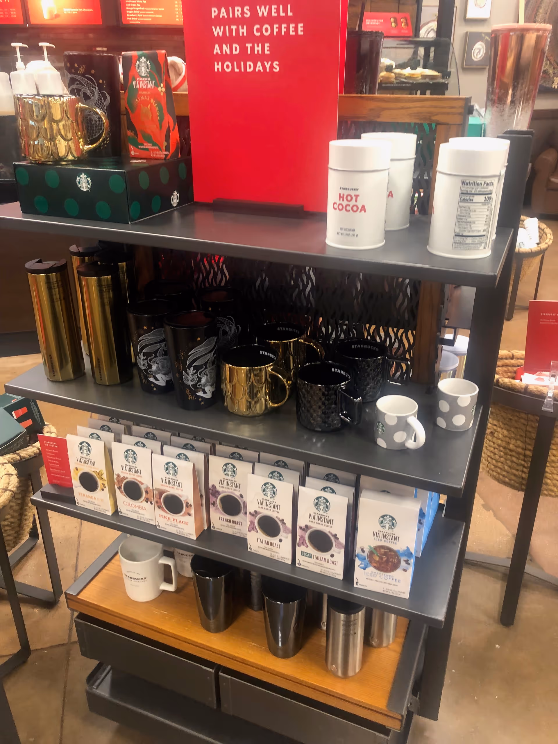 Multi-tier display shelf featuring coffee mugs, VIA instant boxes, and hot cocoa canisters.