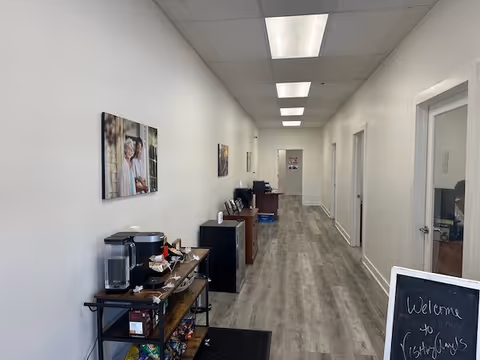 A long, well-lit hallway with a coffee station and framed photographs along the wall.