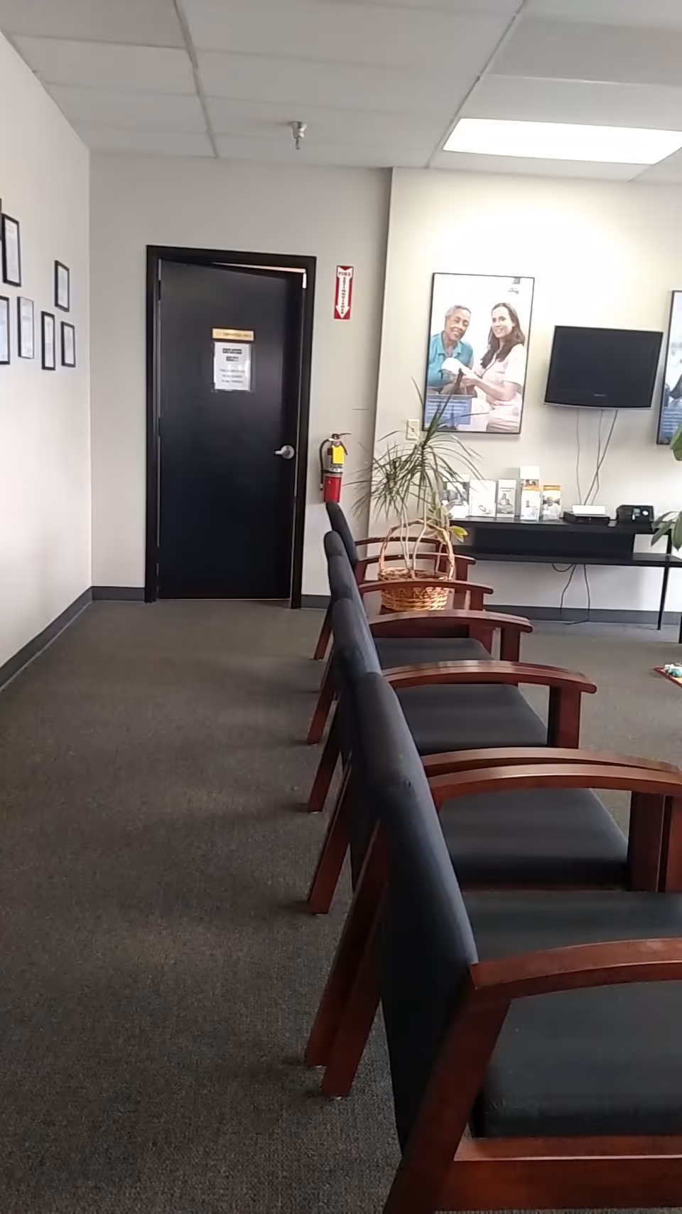 A waiting area with row chairs, a door, plant, and wall posters.