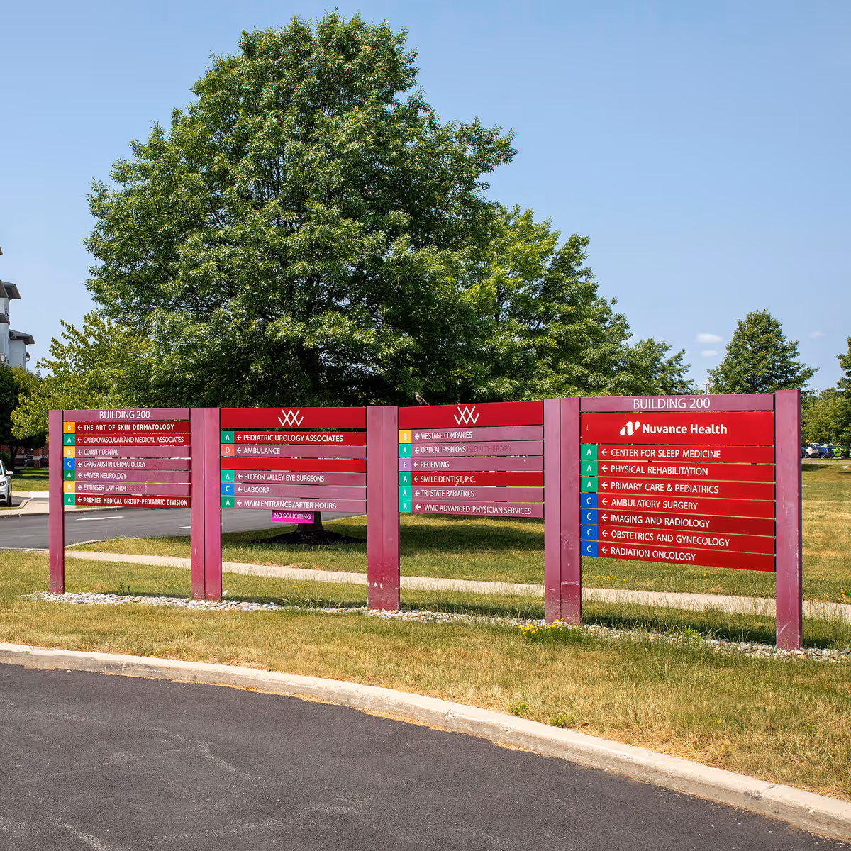 Magenta outdoor sign panels with Nuvance Health directory beside a large tree.