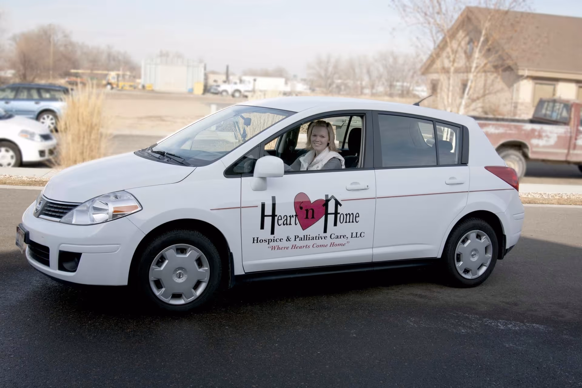 White Heart 'n Home Hospice van outdoors with driver smiling inside and logo visible.