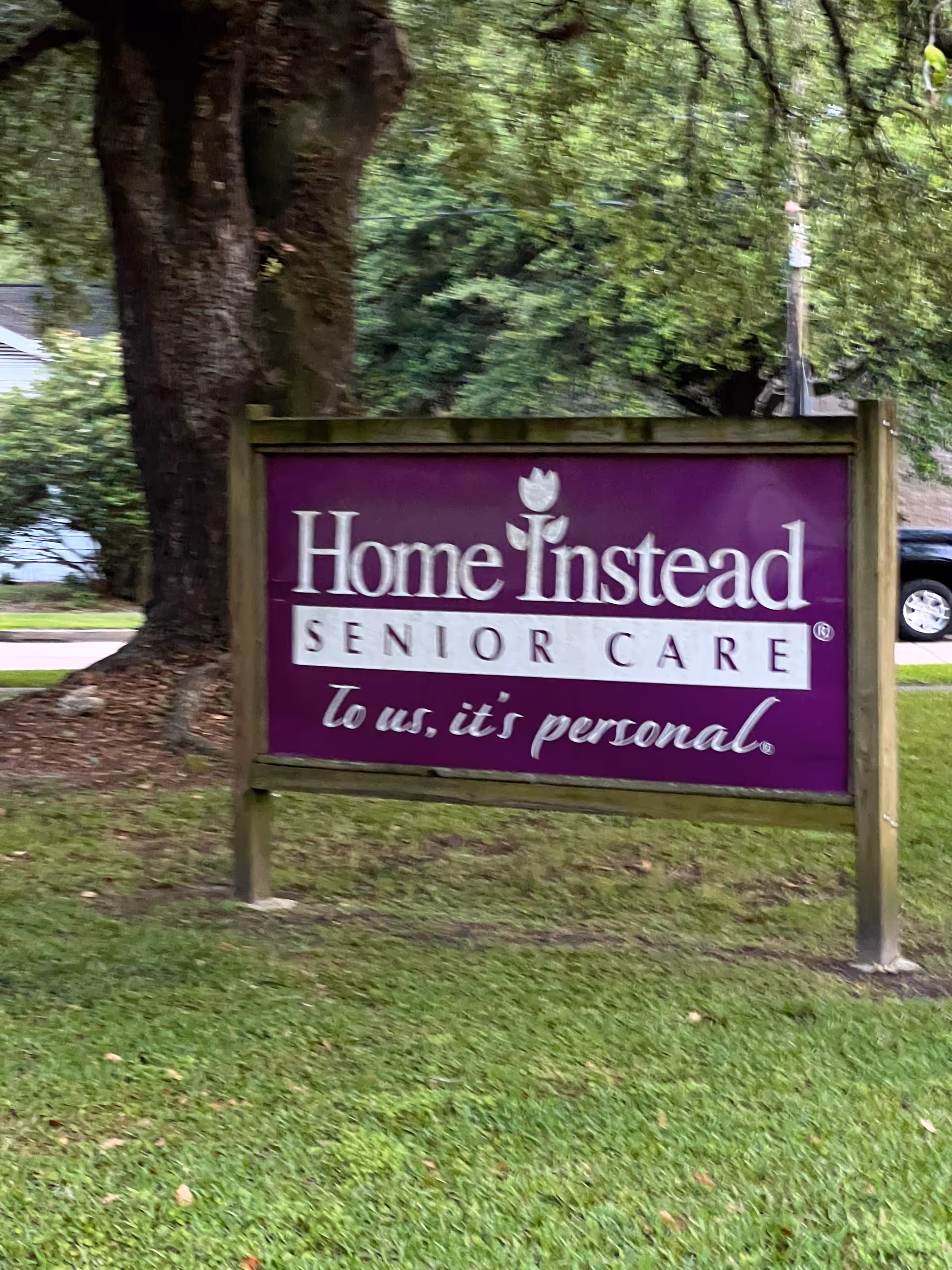 Purple Home Instead Senior Care sign on a wooden frame in a grassy yard