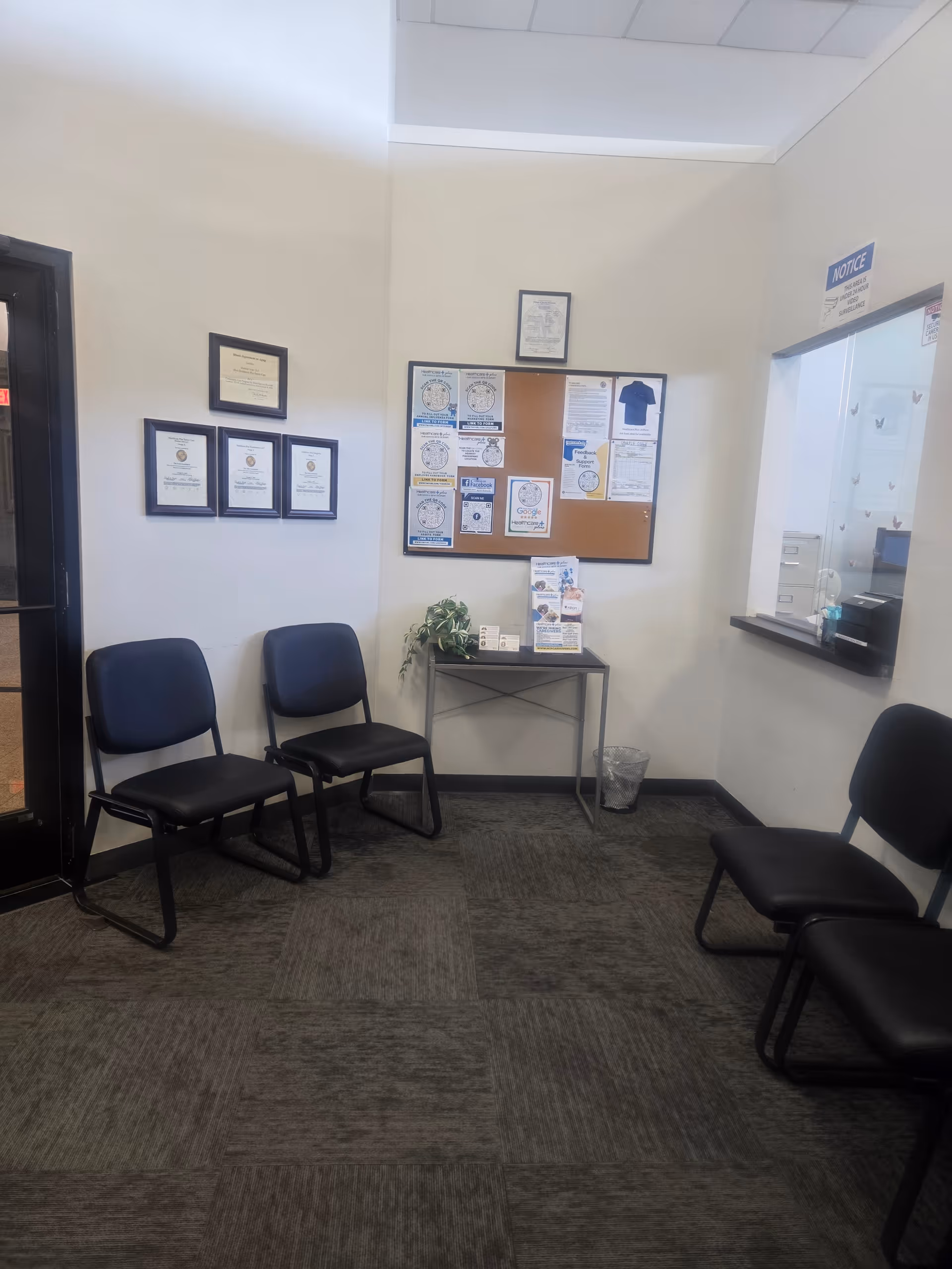A small interior waiting area with blue chairs, a bulletin board, and a reception window.