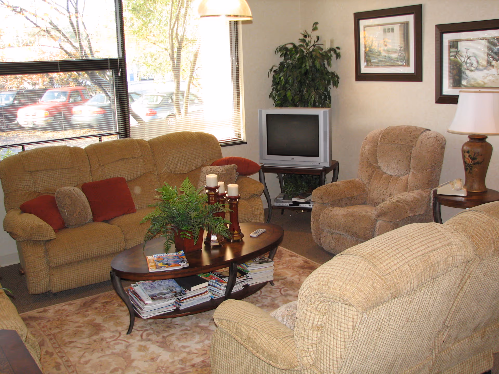 Cozy beige living room with couches, coffee table, TV, plants, and magazines.